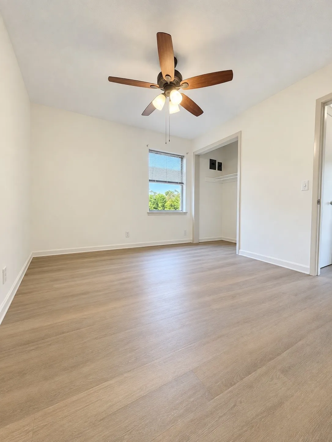 Wood-finish flooring, ceiling fan with integrated lighting, window with exterior scenery, and recessed closet space