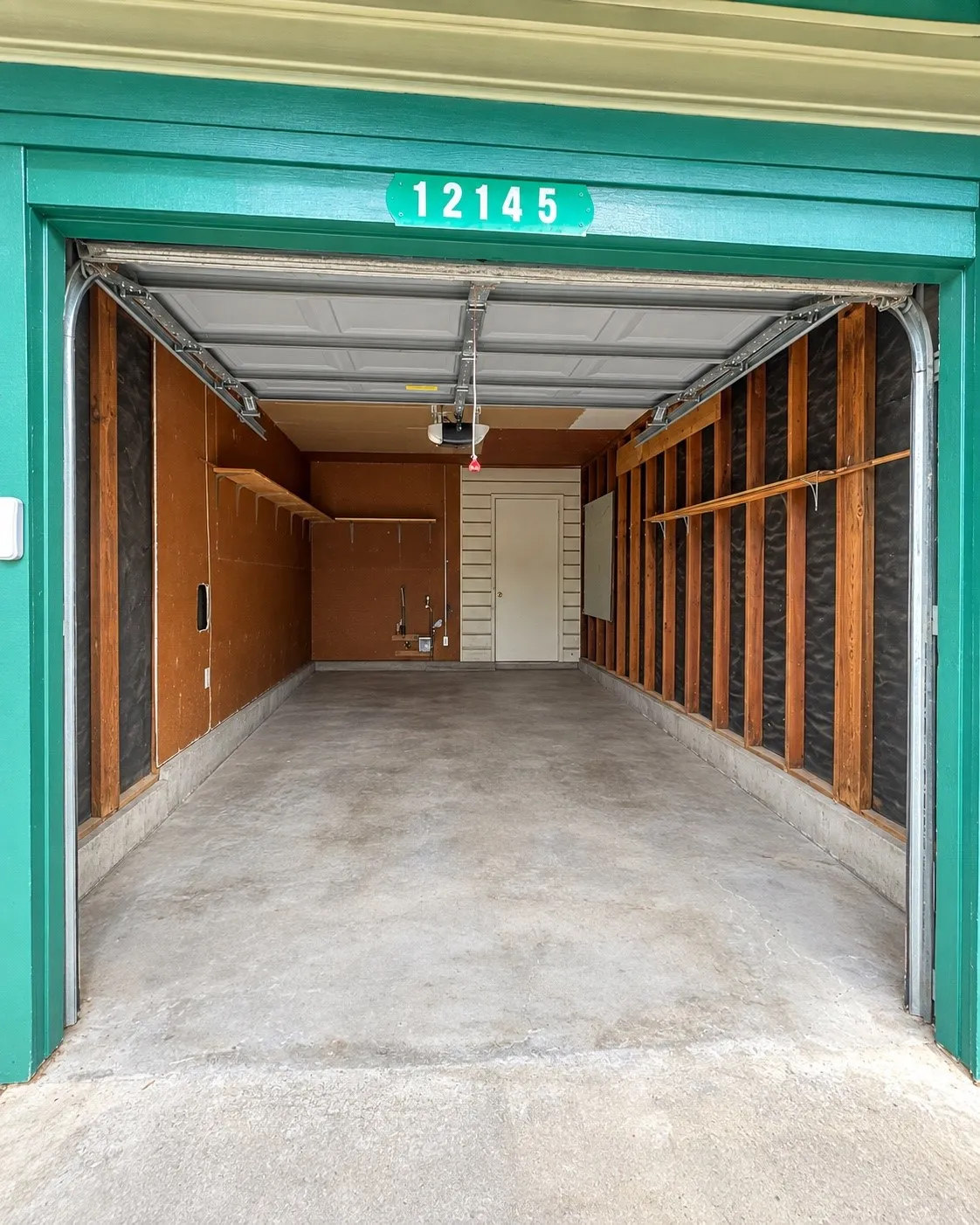 Single-car garage with a concrete floor, built-in shelving, and an overhead door
