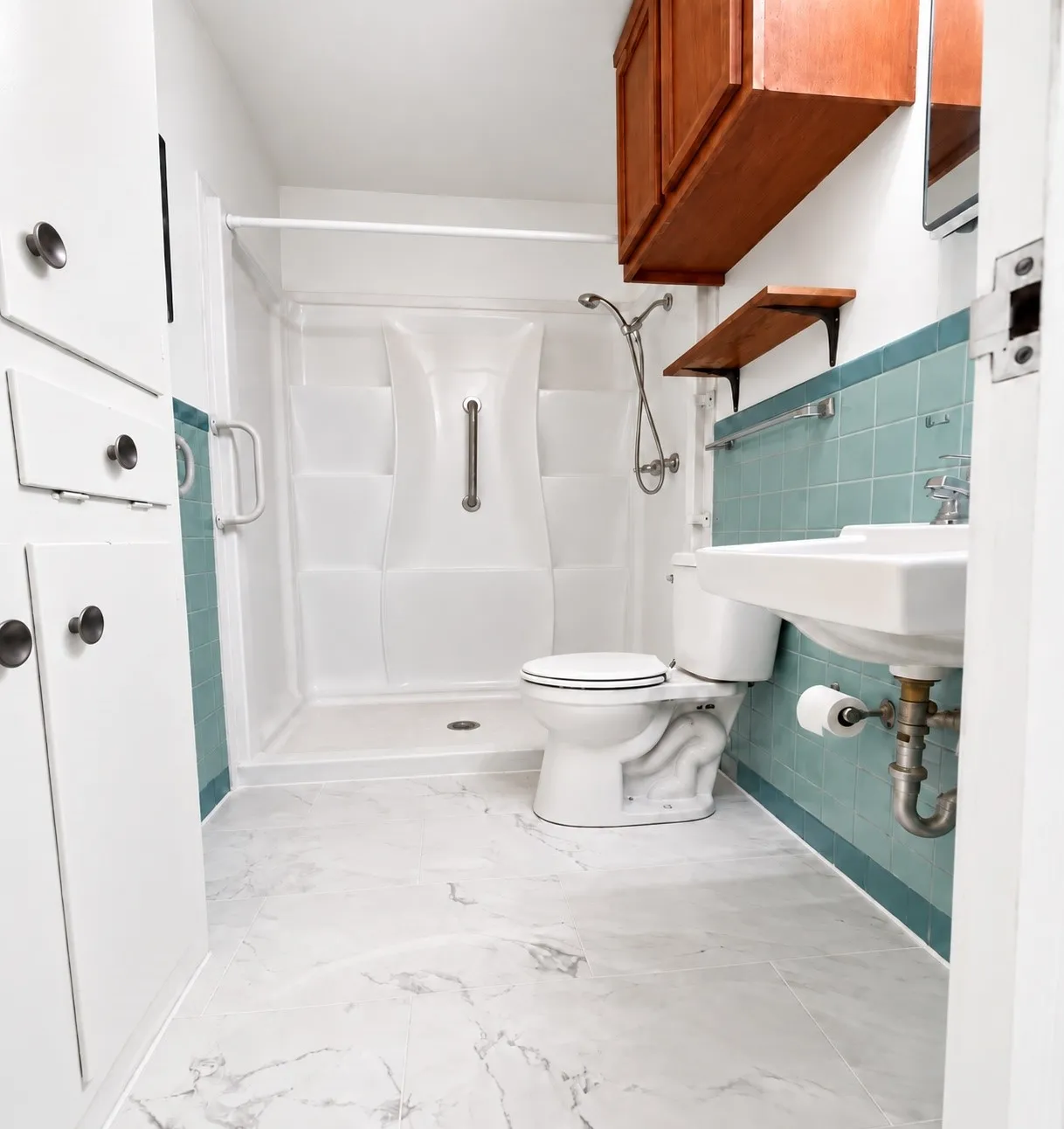 White shower stall with grab bars, wall-mounted sink, white toilet, and tile flooring