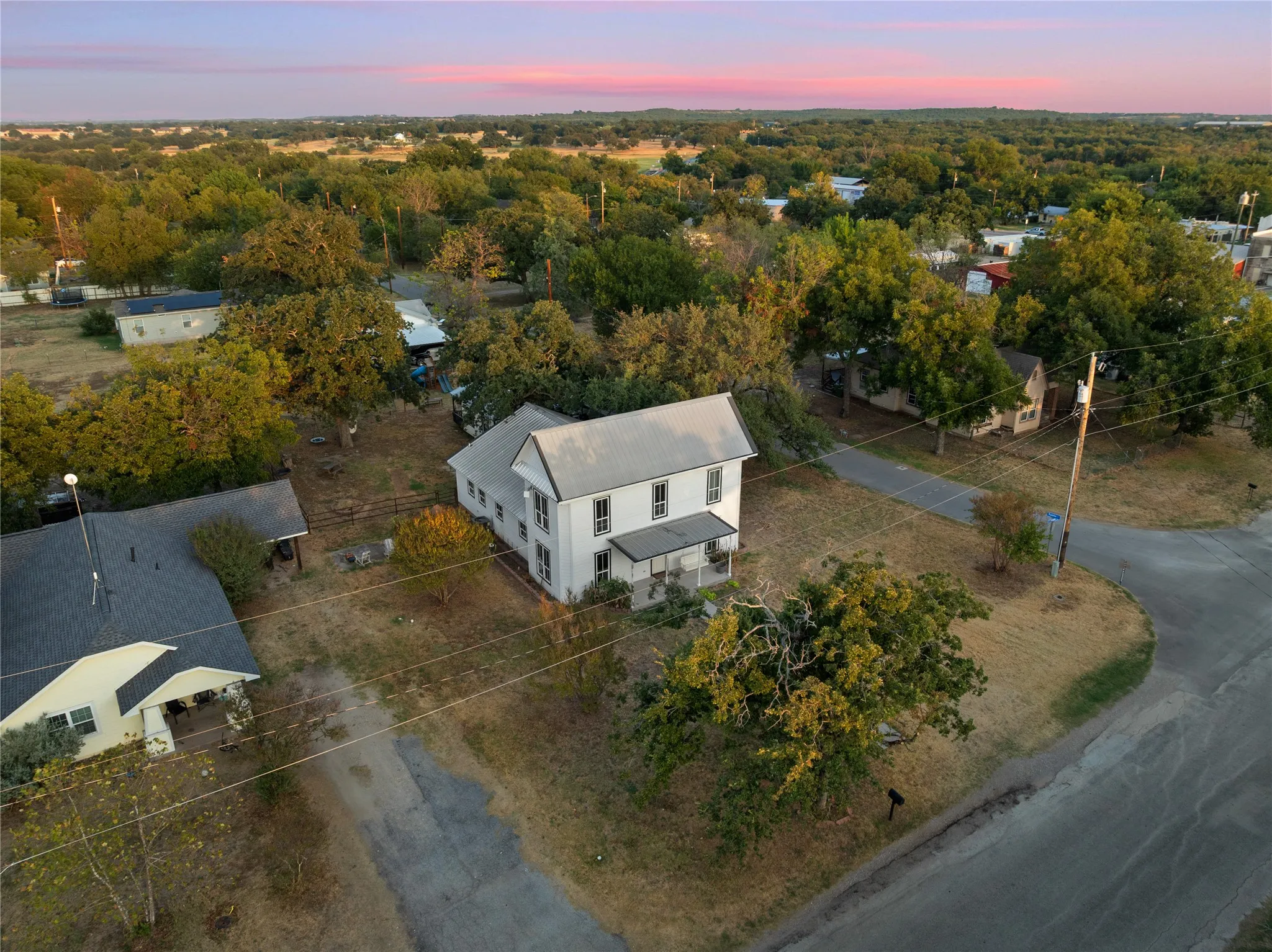 Two-story property with a metal roof, a covered porch, and mature trees