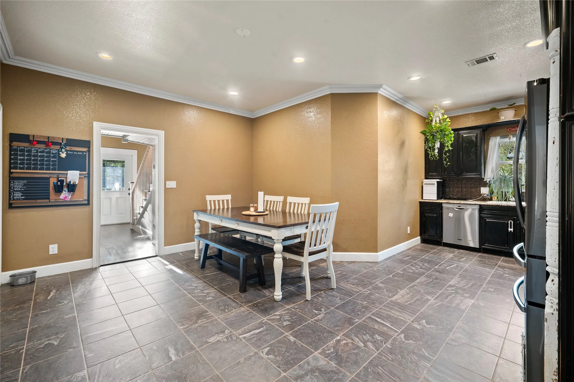 Tile flooring, dark wood-finish cabinetry, stainless steel dishwasher, crown molding, and recessed lighting