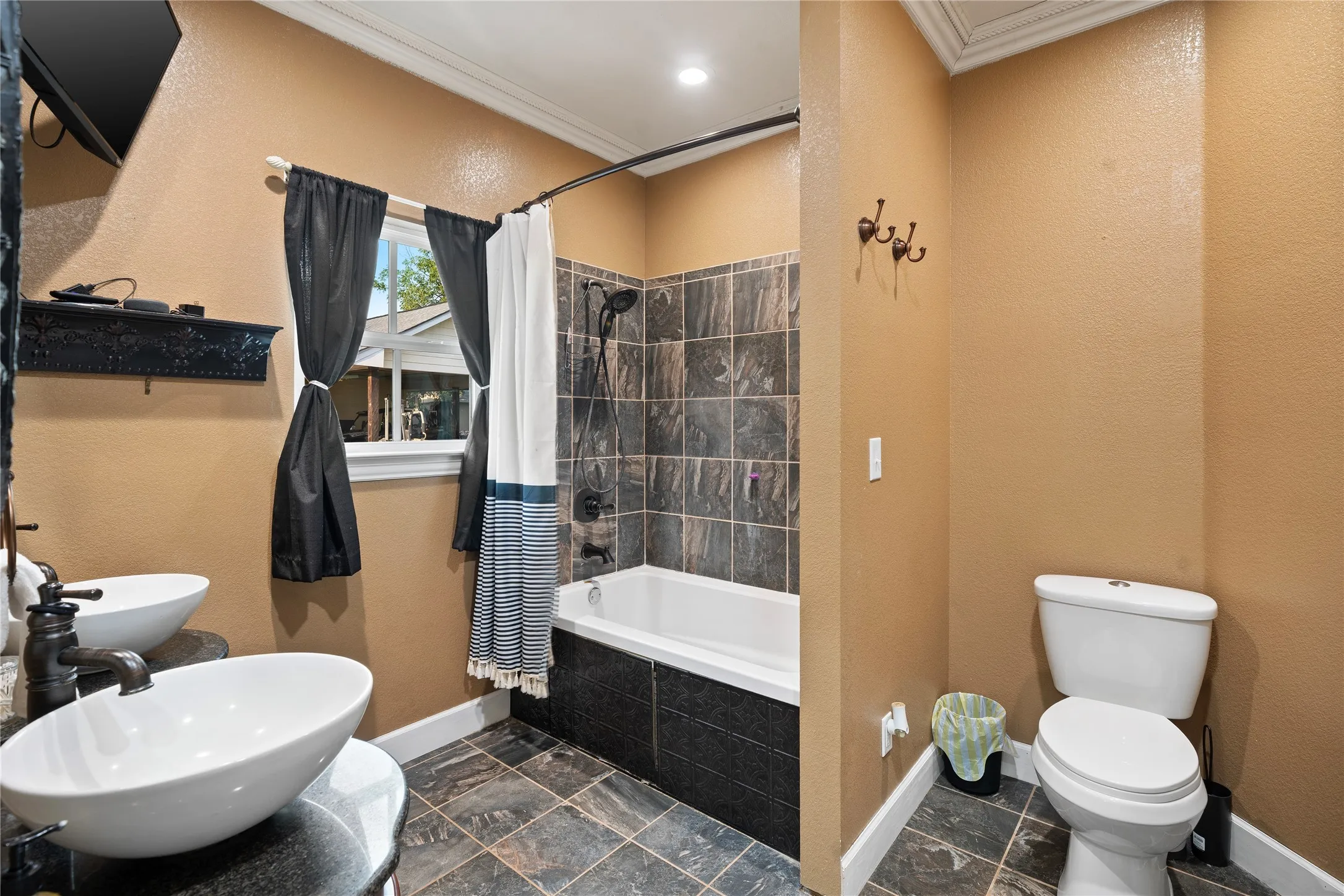 Dual vessel sinks with dark bronze fixtures, integrated bathtub and shower with tile surround, toilet, and tiled flooring