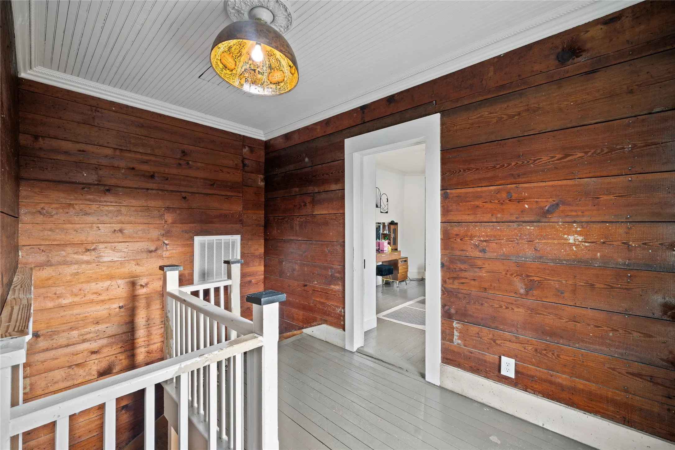 Wood-paneled wall, painted wood-finish flooring, white trim, white railing, and decorative ceiling fixture