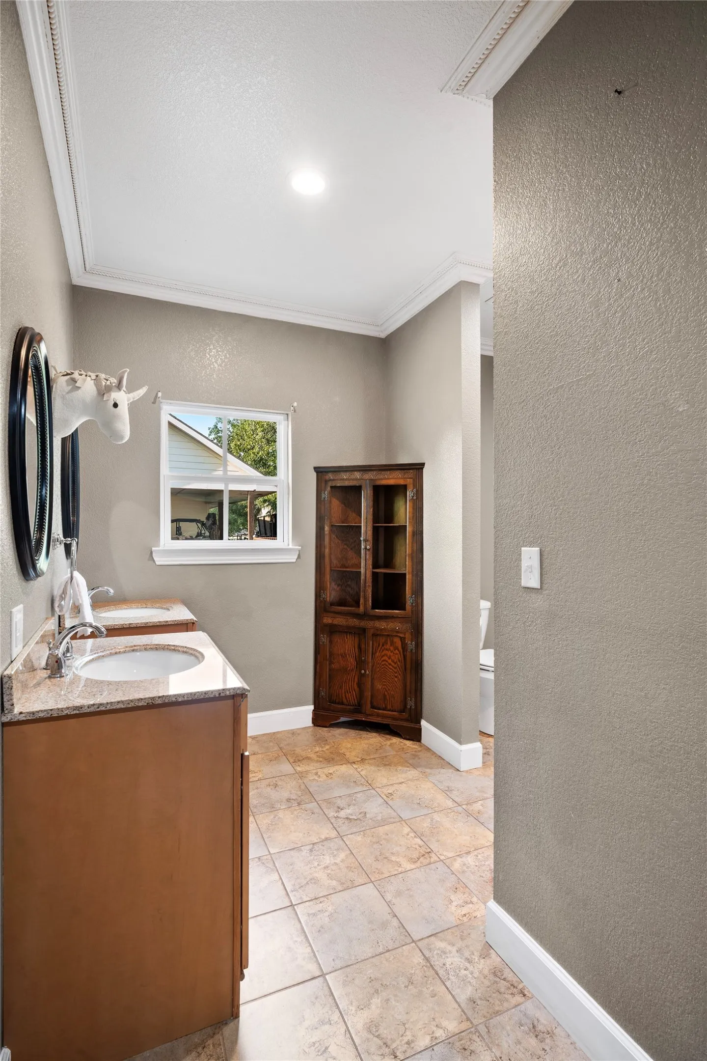 Dual undermount sinks, stone-finish countertop, wood-finish cabinetry, tile flooring, and crown molding