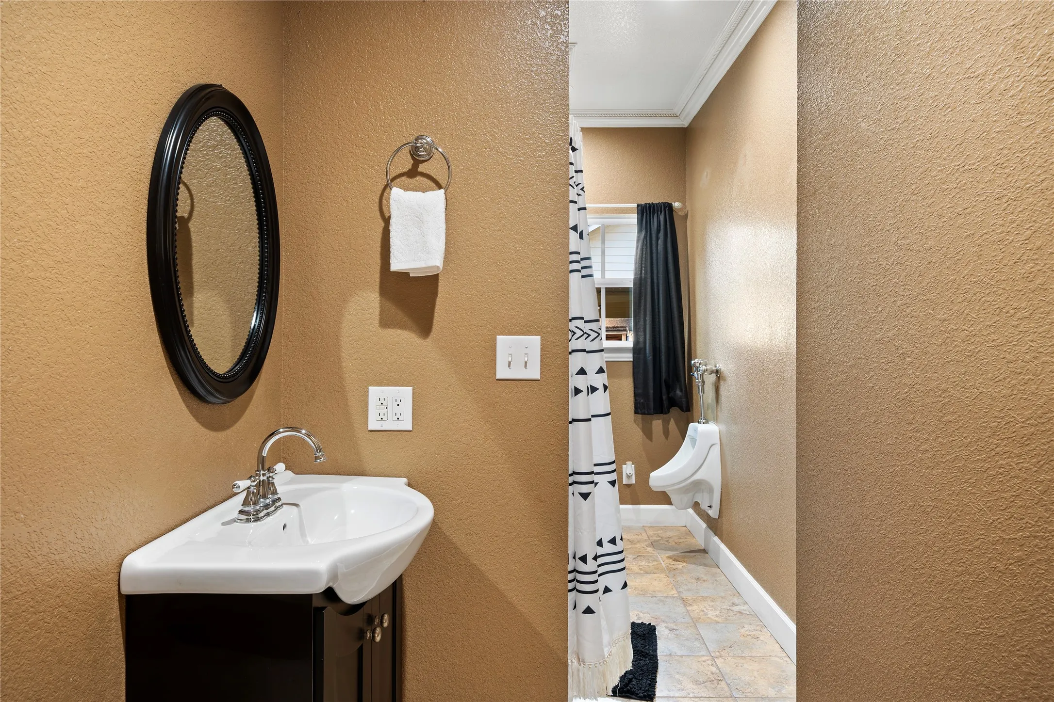 Corner pedestal sink with chrome faucet, black vanity, and oval framed mirror
