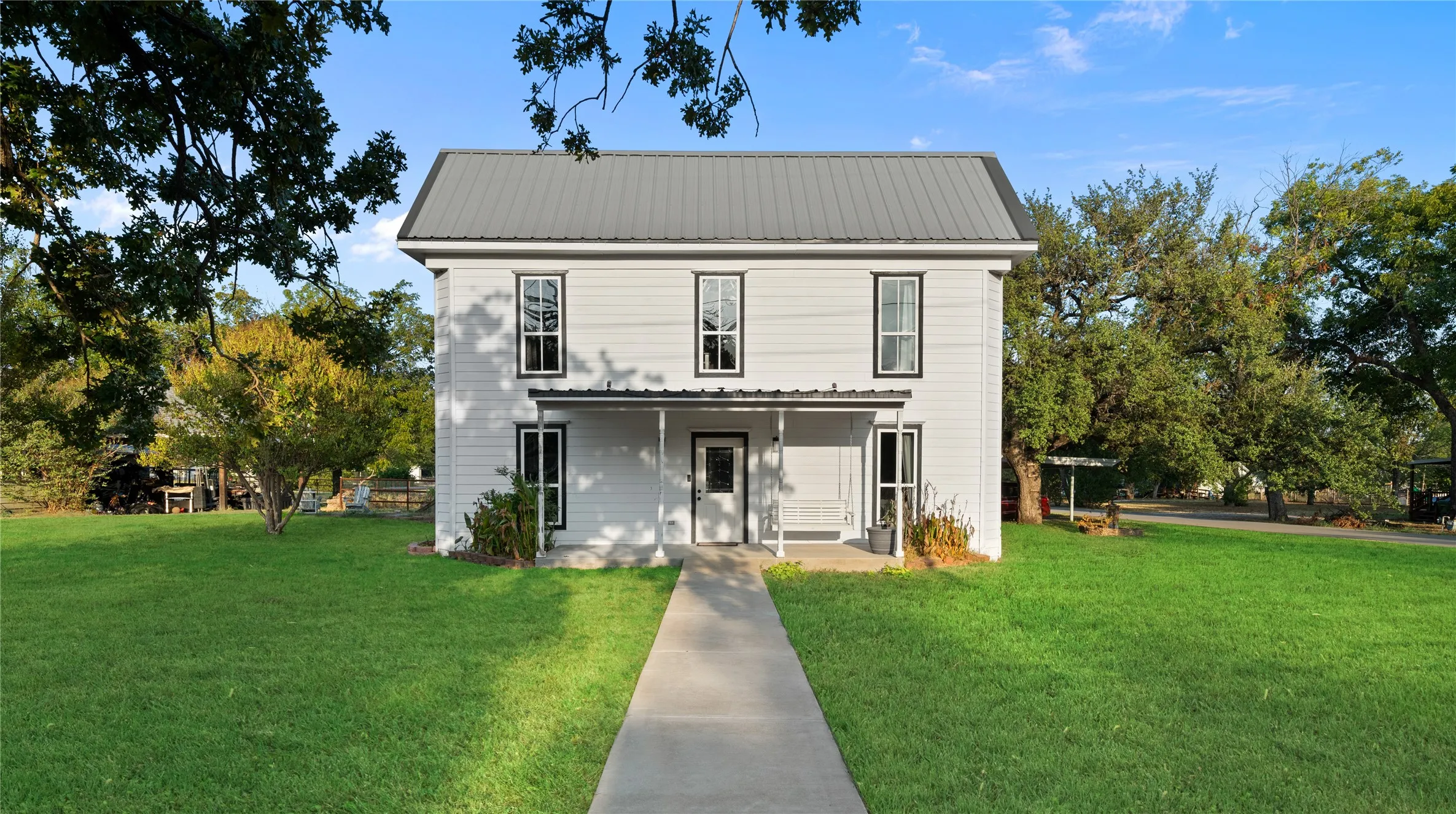 Two-story residence featuring white siding, a metal roof, and a covered front porch with columns