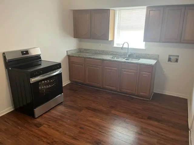 Stainless steel range, wood-finish flooring, wood cabinetry, granite-finish countertops, and a double basin sink