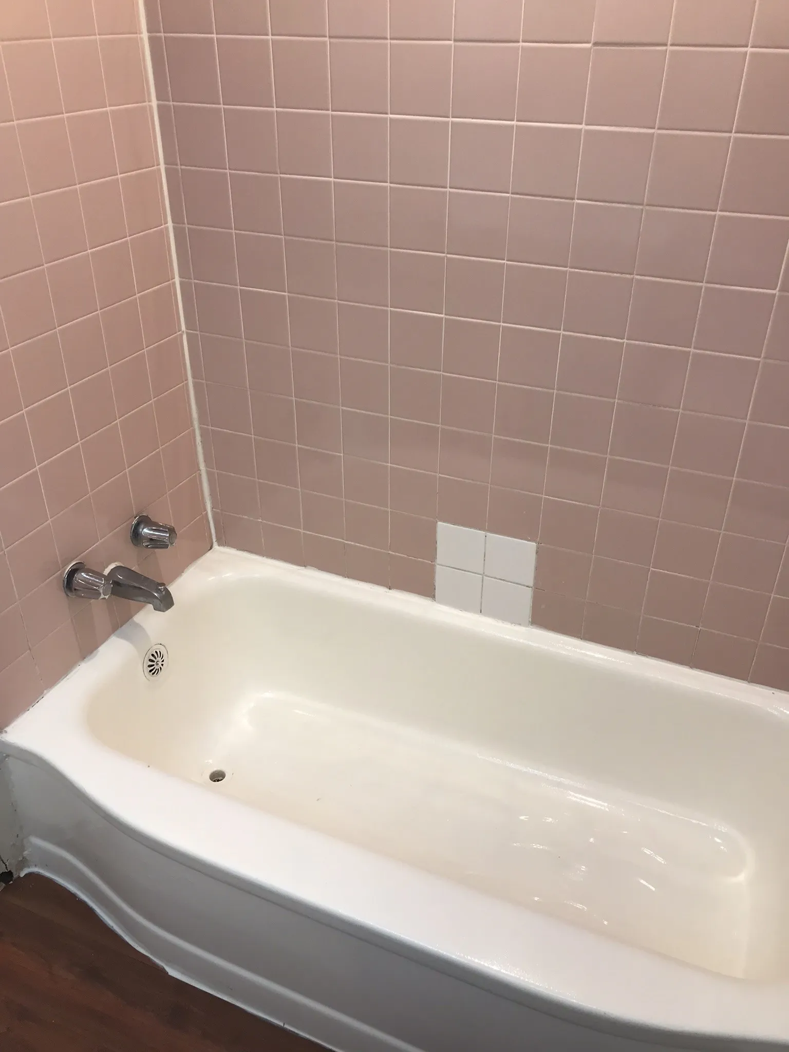 White bathtub with chrome fixtures and pink square wall tiles
