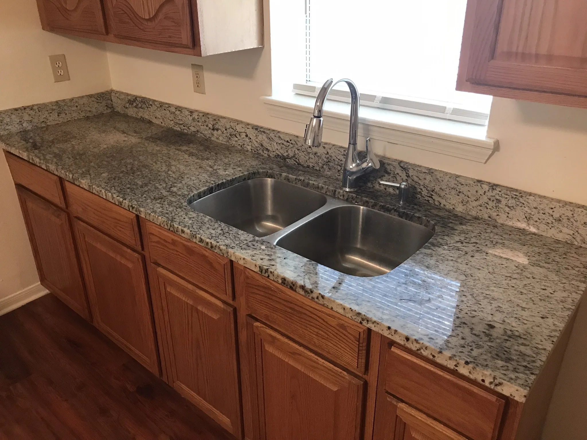 Wood-finish cabinetry paired with a durable stone countertop, stainless steel double-basin sink, and a chrome pull-down faucet