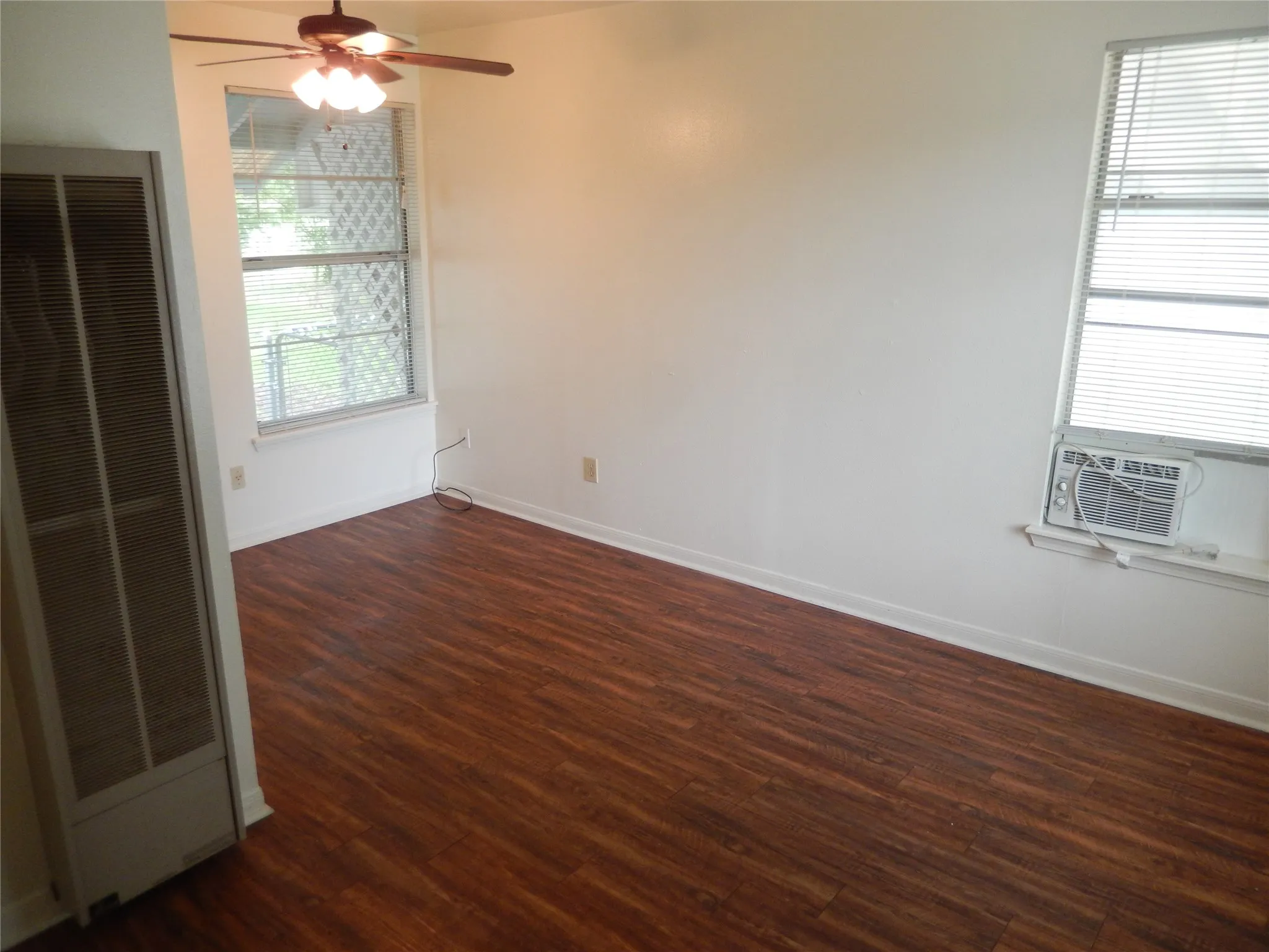 Wood-finish flooring, ceiling fan, and white walls with window blinds