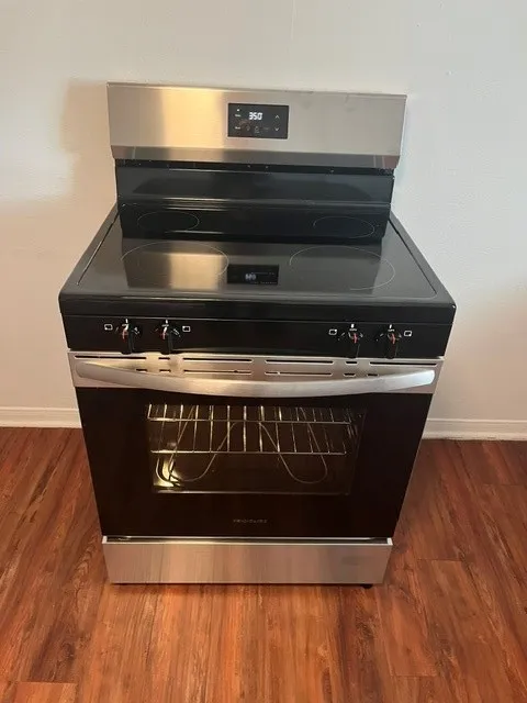 Stainless steel oven with a glass cooktop, digital display, and wood-finish flooring