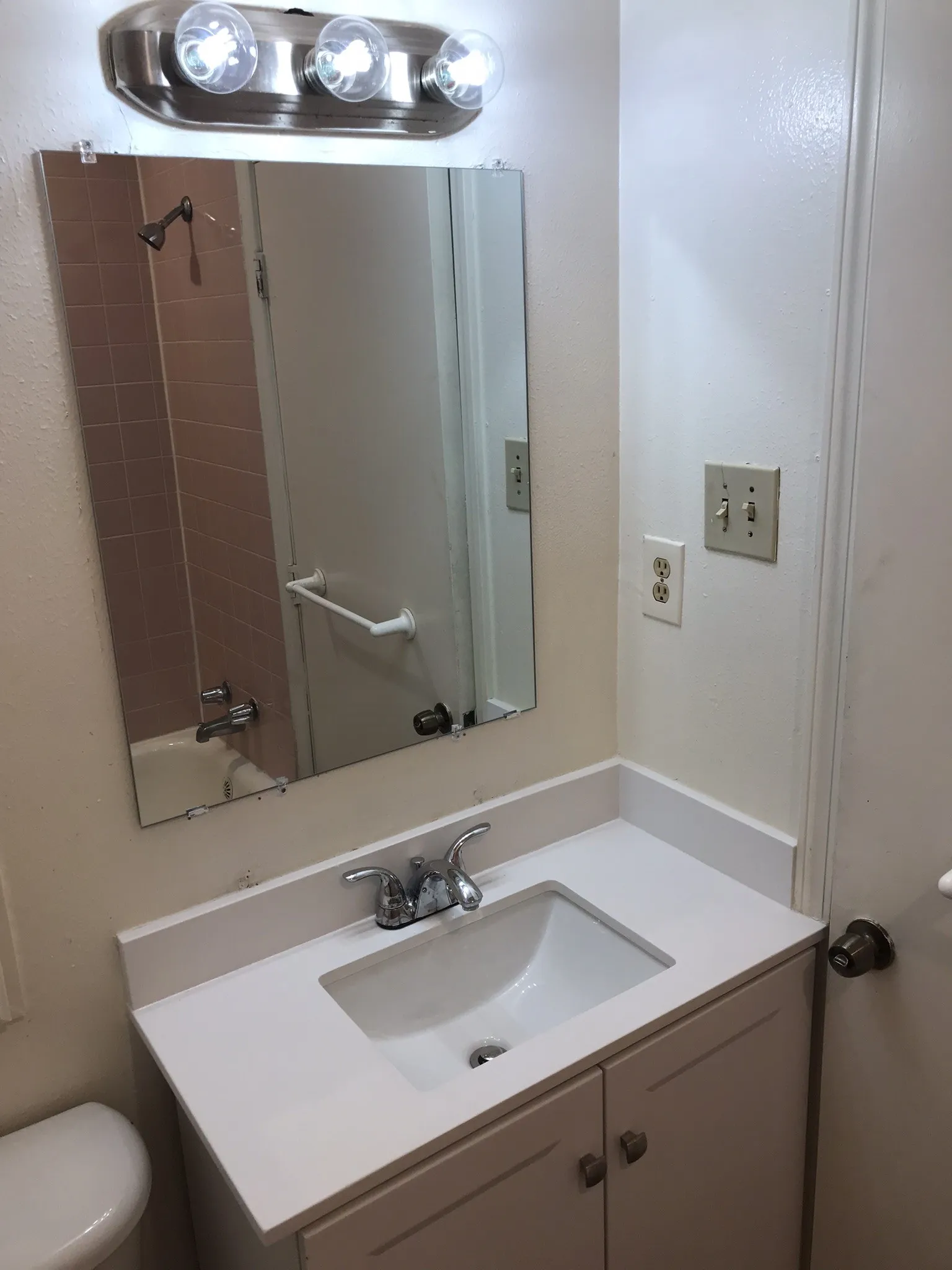 Vanity with integrated sink, chrome faucet, wall-mounted mirror, and overhead vanity lighting