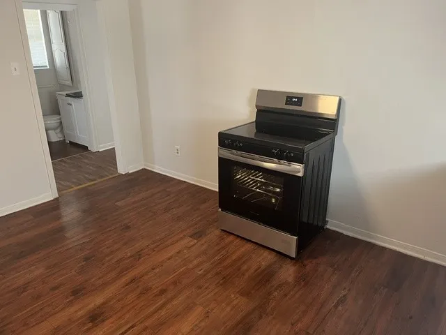 Stainless steel and black range with a glass cooktop, wood-finish flooring, and light-toned walls