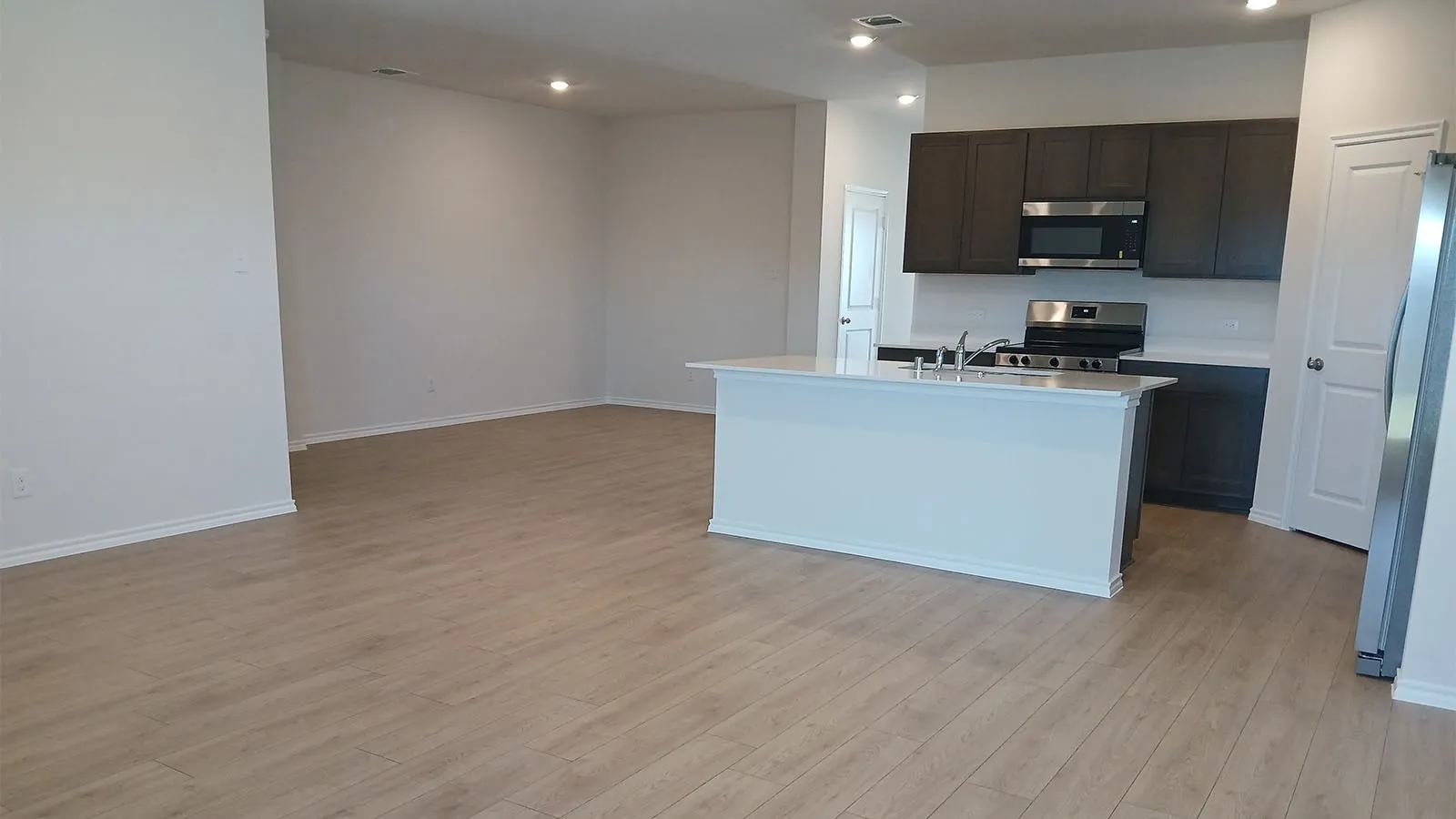Spacious kitchen featuring dark wood-finish cabinetry, stainless steel appliances, a white island with an integrated sink, and light wood-finish flooring
