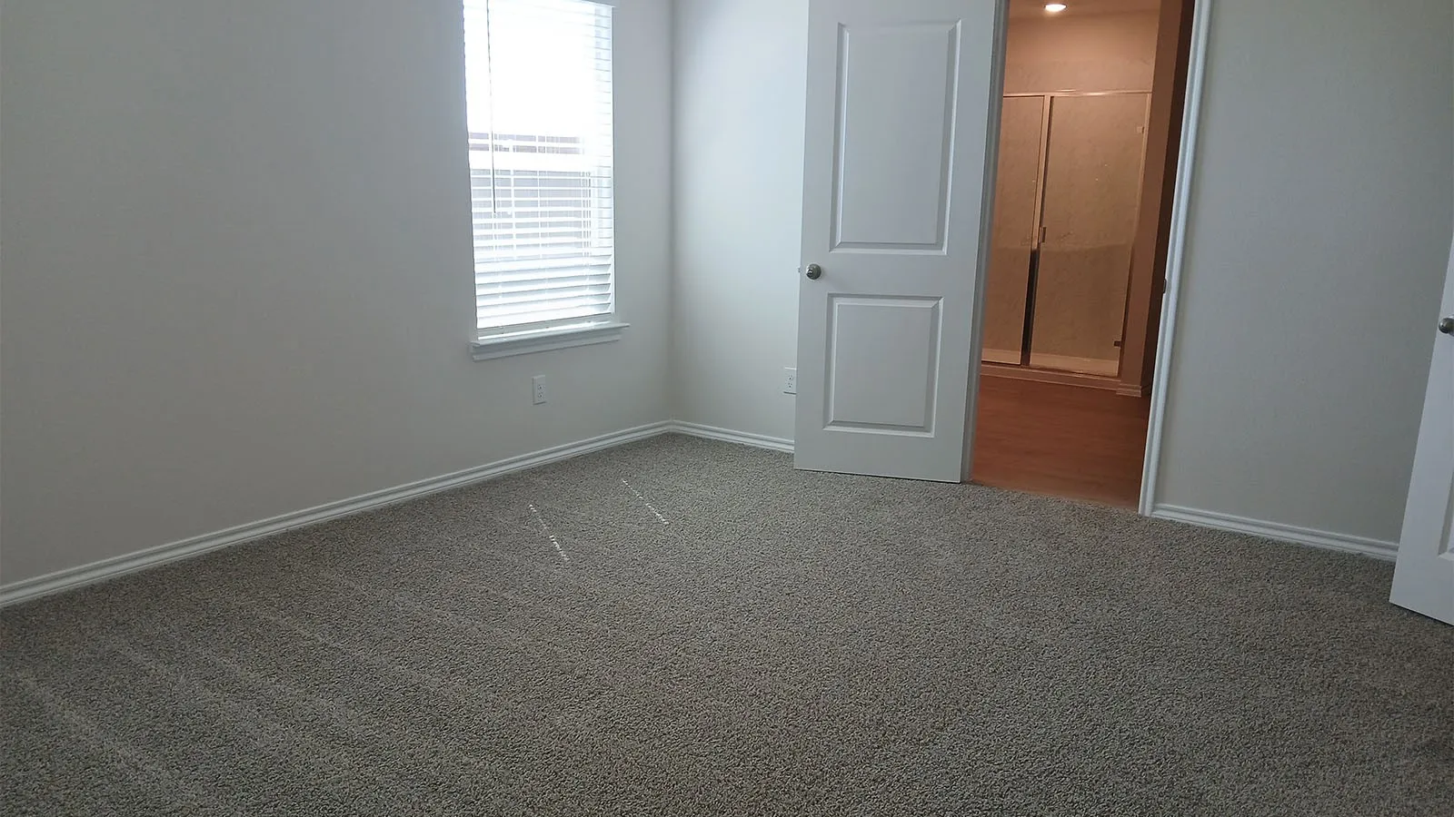 Neutral carpet flooring, white painted walls, window with blinds, and white interior doors