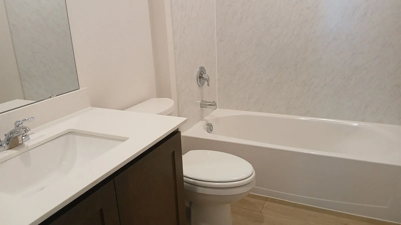 Vanity with integrated sink, white countertop, dark wood-finish cabinetry, chrome fixtures, and a white bathtub with tile-look surround