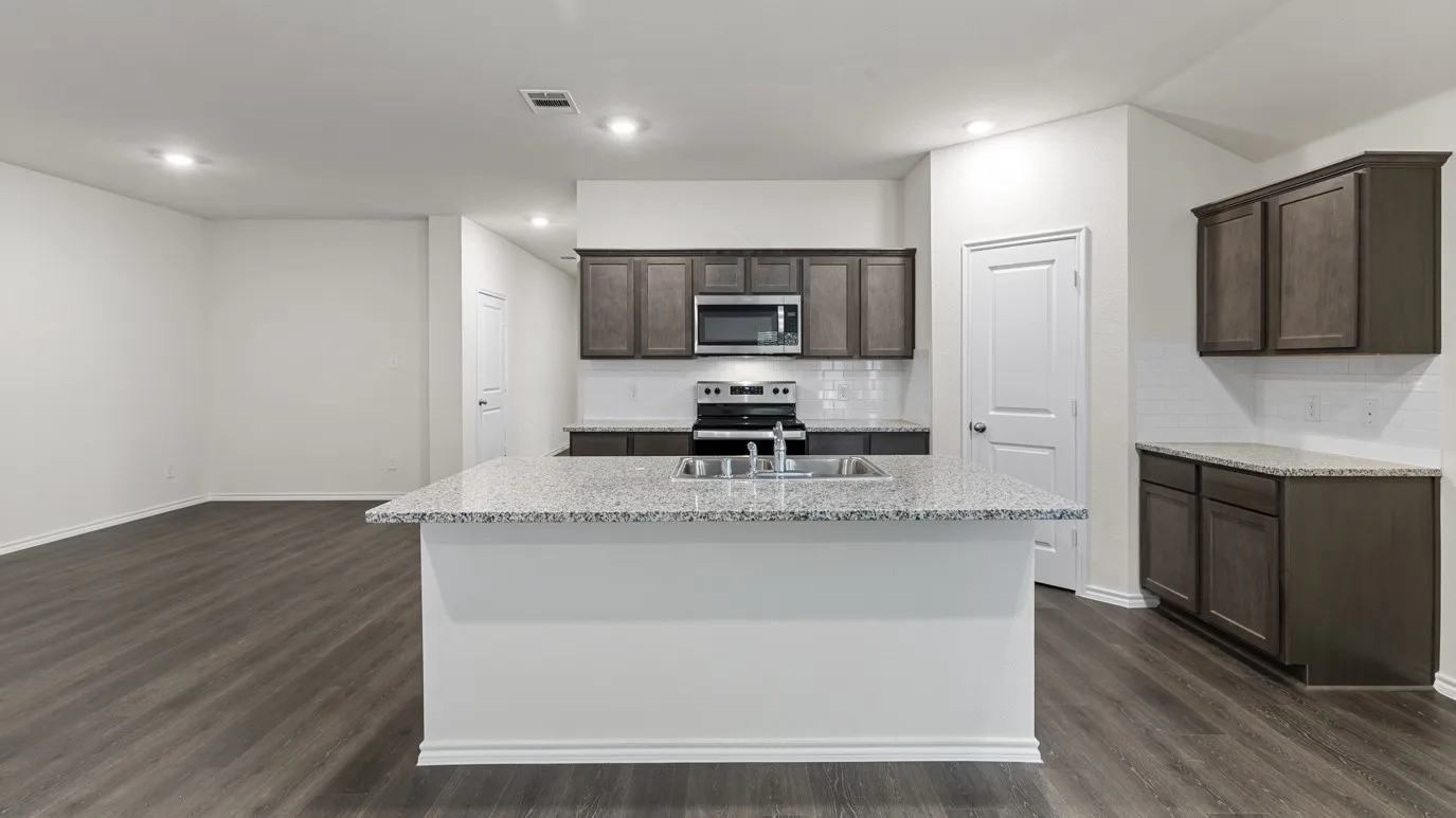 Open-concept kitchen featuring an island with a stainless steel sink, dark wood-finish cabinetry, light-colored countertops, and stainless steel appliances