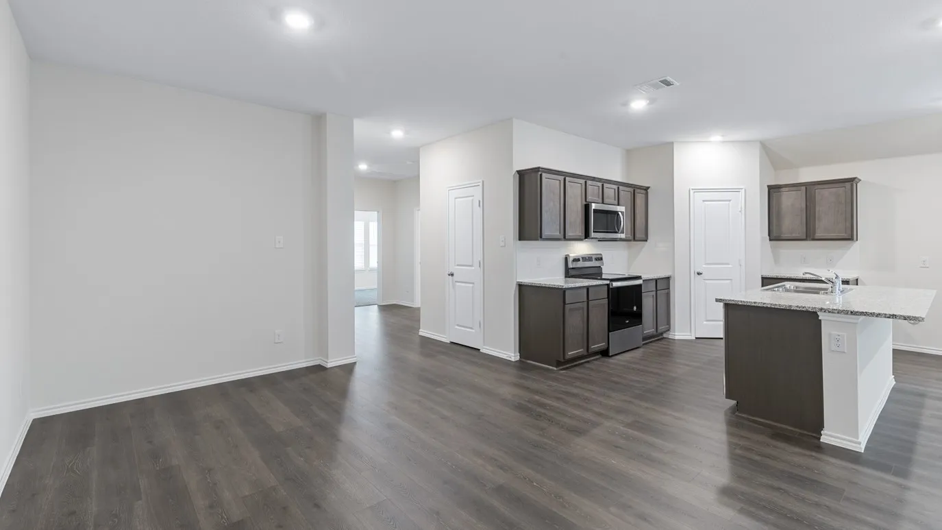 Open-concept living space with dark wood-finish flooring, recessed lighting, and a kitchen featuring dark cabinetry, stainless steel appliances, and a central island with a light-toned countertop