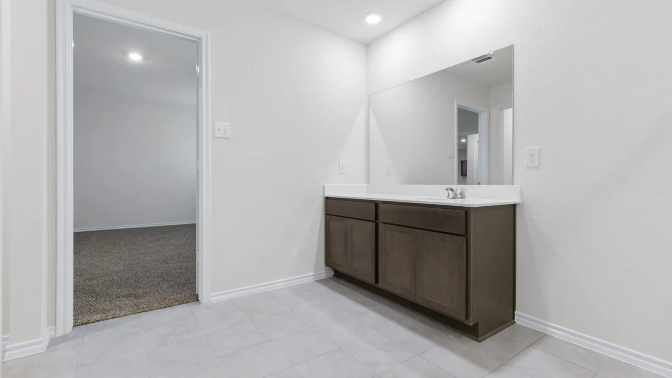 Spa-inspired primary bathroom featuring a wood-finish vanity with dual sink configuration, white quartz countertop, and large framed mirror with integrated lighting