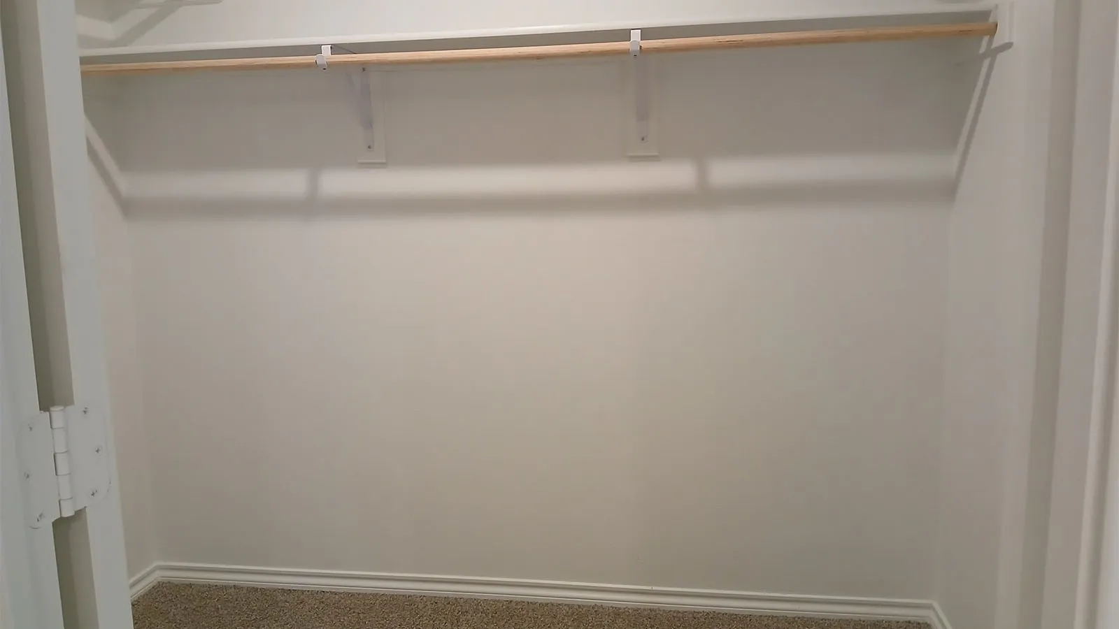 Carpeted closet with a single hanging rod and shelf