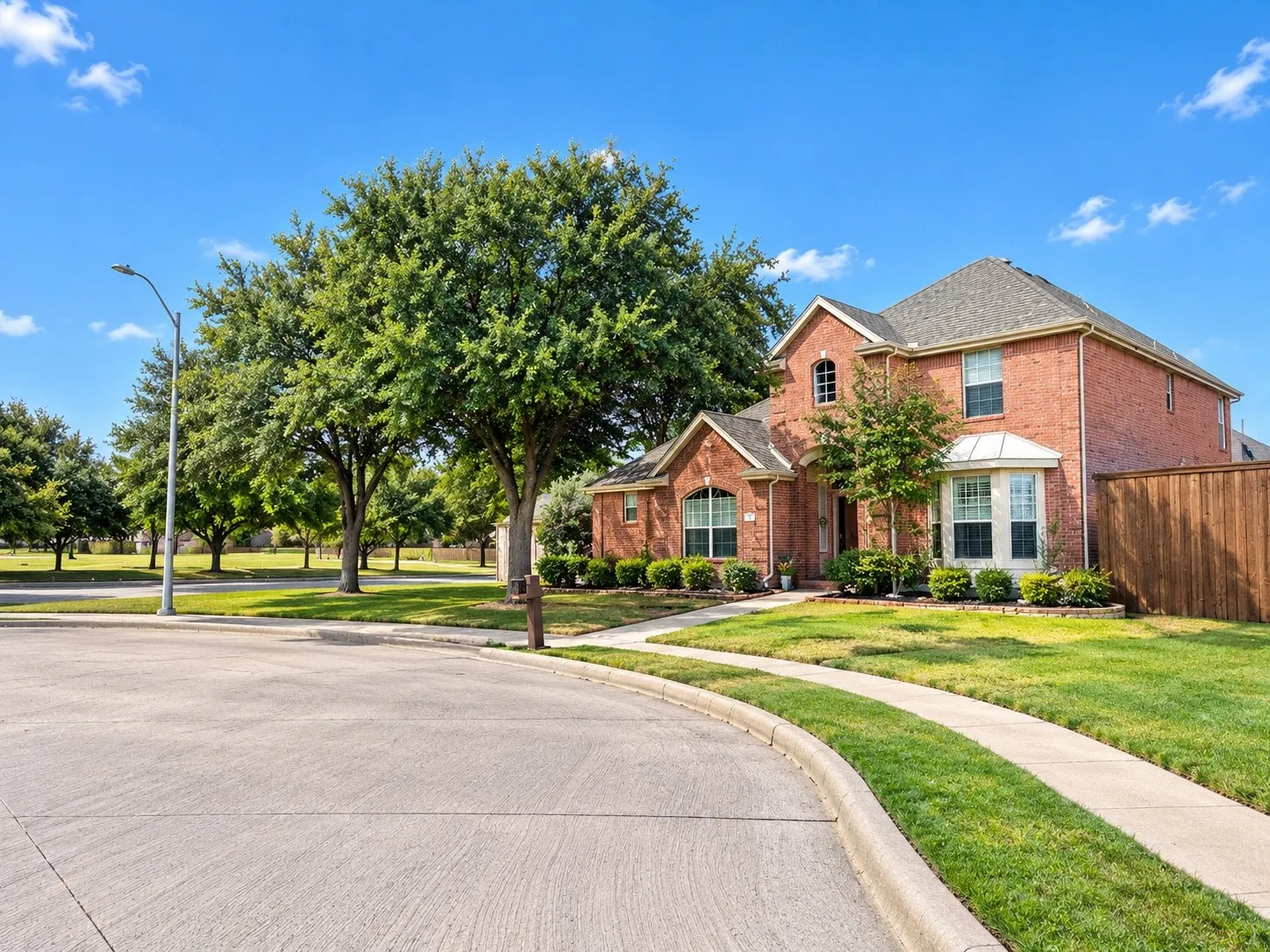 Brick exterior construction, prominent bay window, established landscaping, concrete sidewalks, and a wooden privacy fence