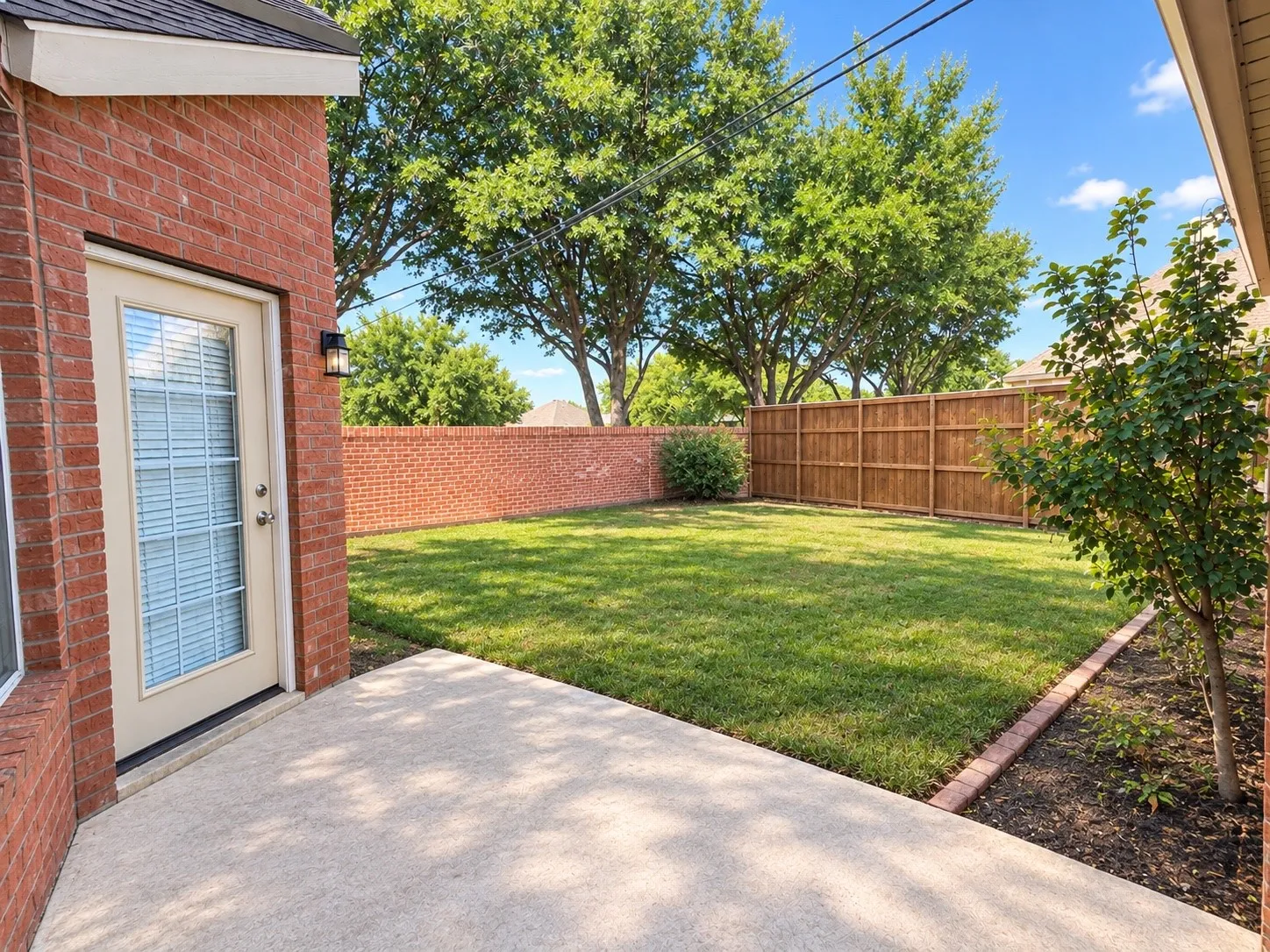 Private backyard featuring a concrete patio, brick exterior, wood fence, and mature trees