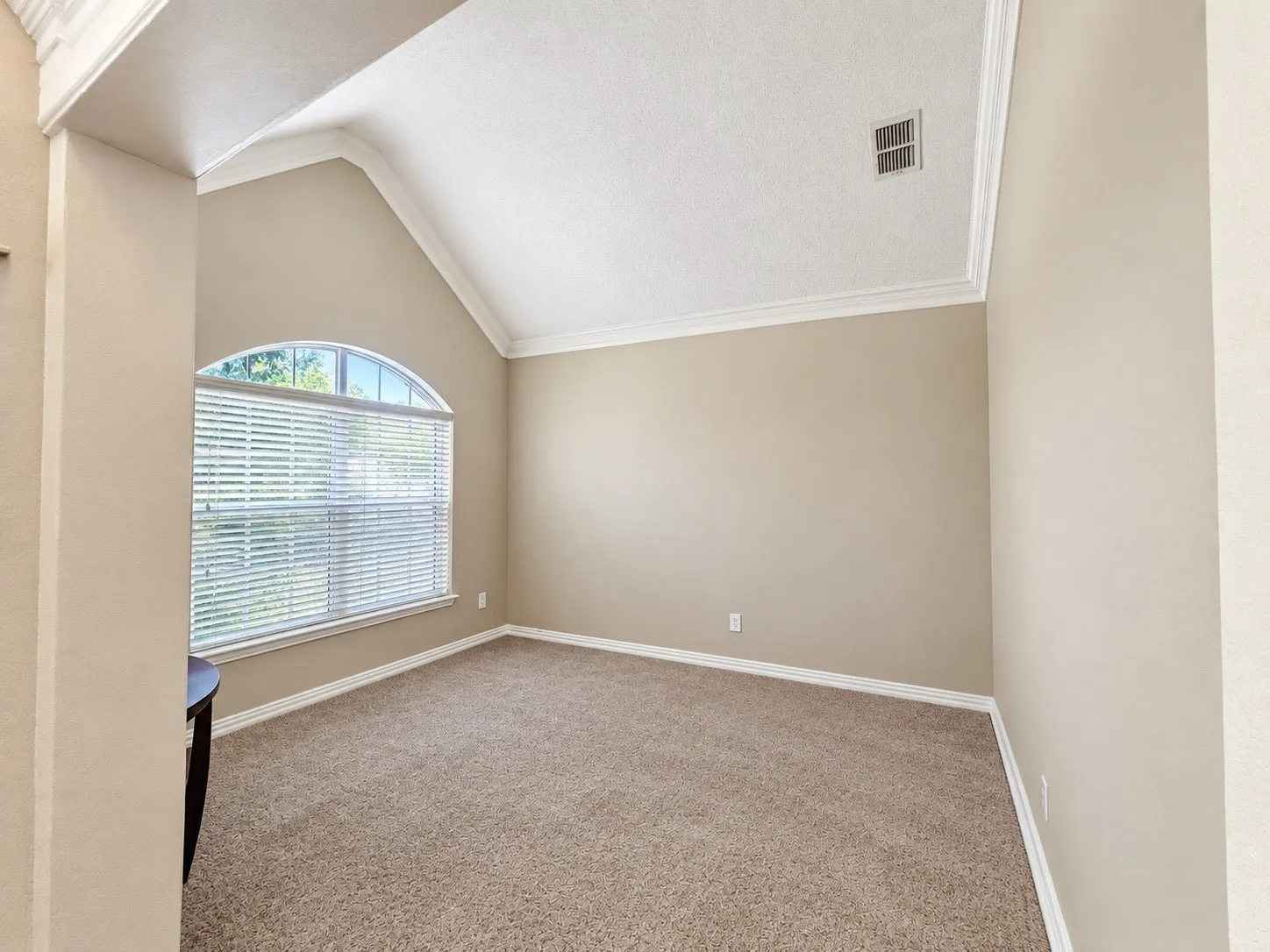 Vaulted ceiling, arched window with blinds, crown molding, and neutral-toned carpeting