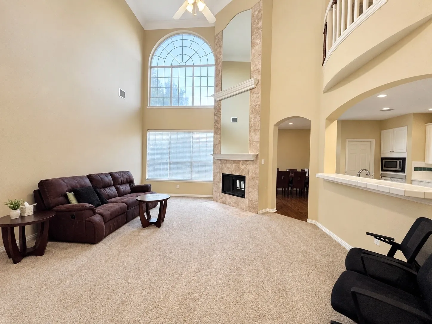 Two-story living area featuring a prominent arched window, fireplace with stone surround, and ceiling fan