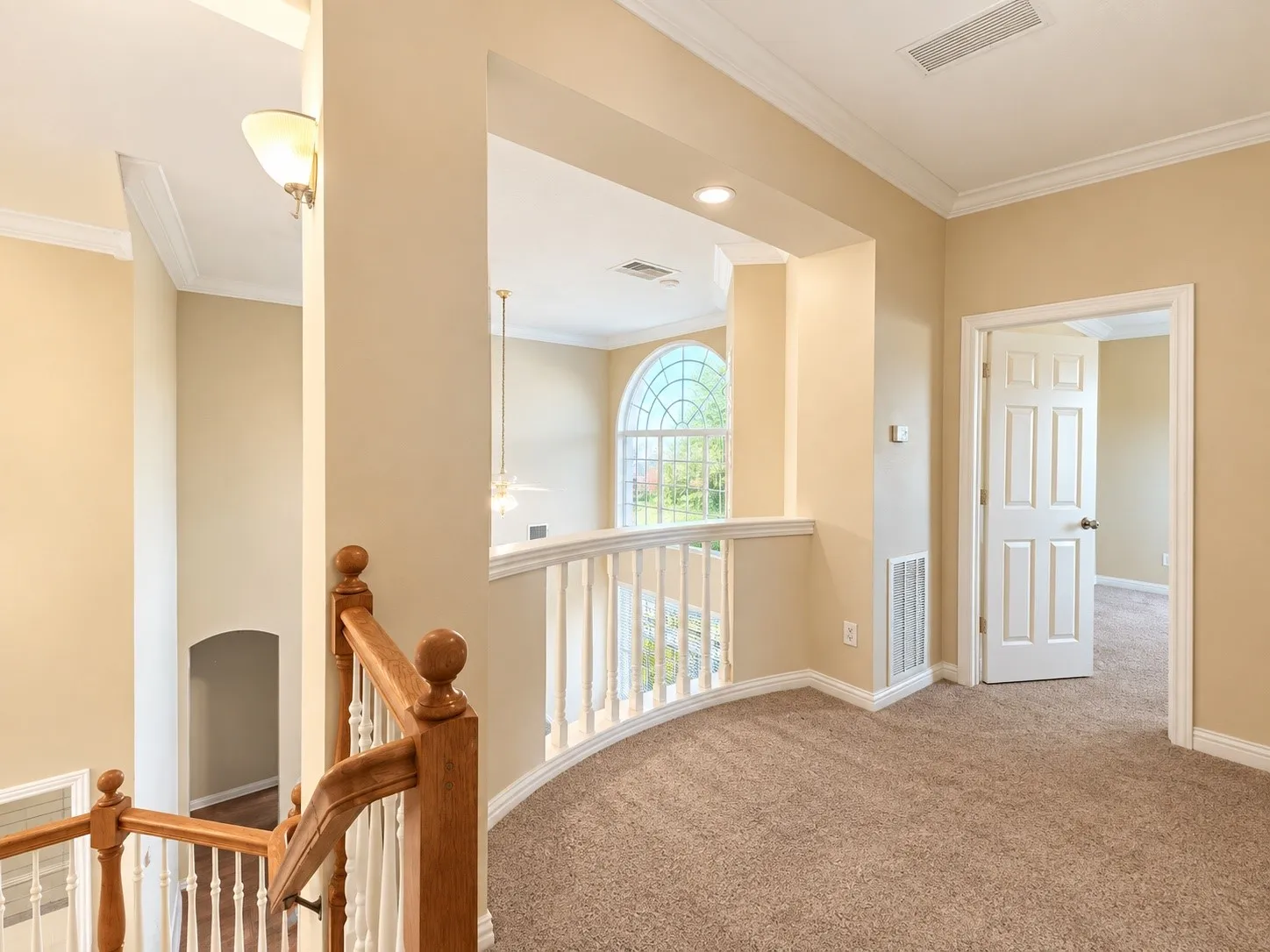 Carpeted loft area featuring a curved railing, a paneled interior door, and crown molding
