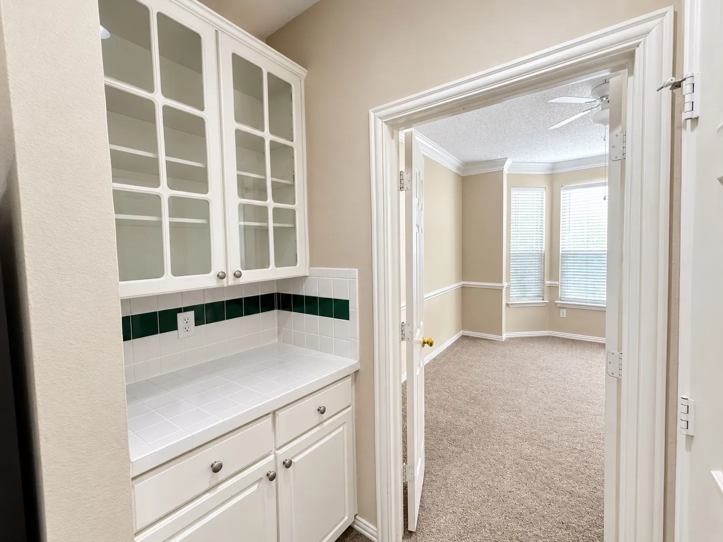 Built-in cabinetry with glass-front uppers and lower storage, tiled countertop, and a decorative tile backsplash