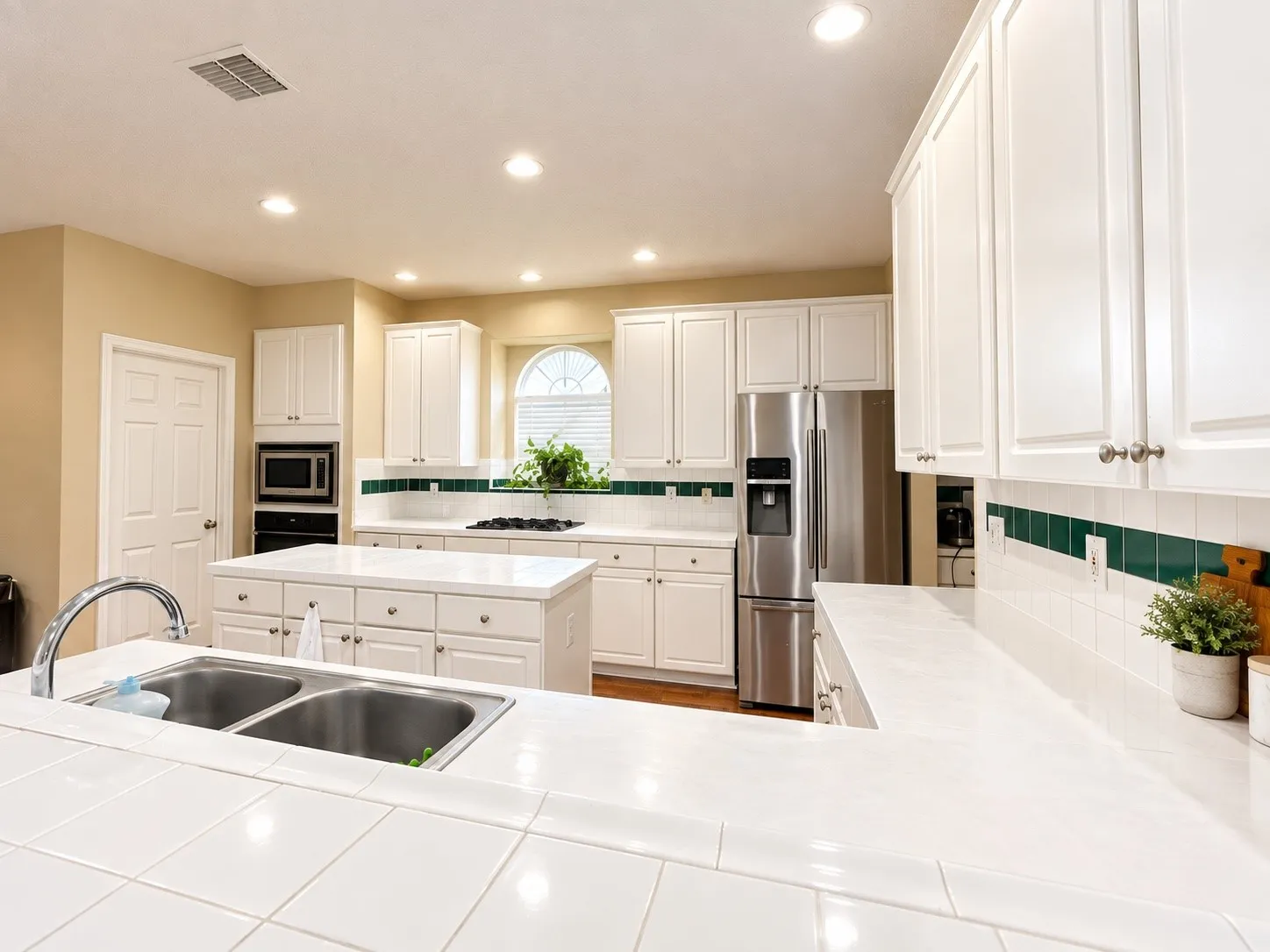 White cabinetry, tile countertops, stainless steel appliances, recessed lighting, and a kitchen island with storage