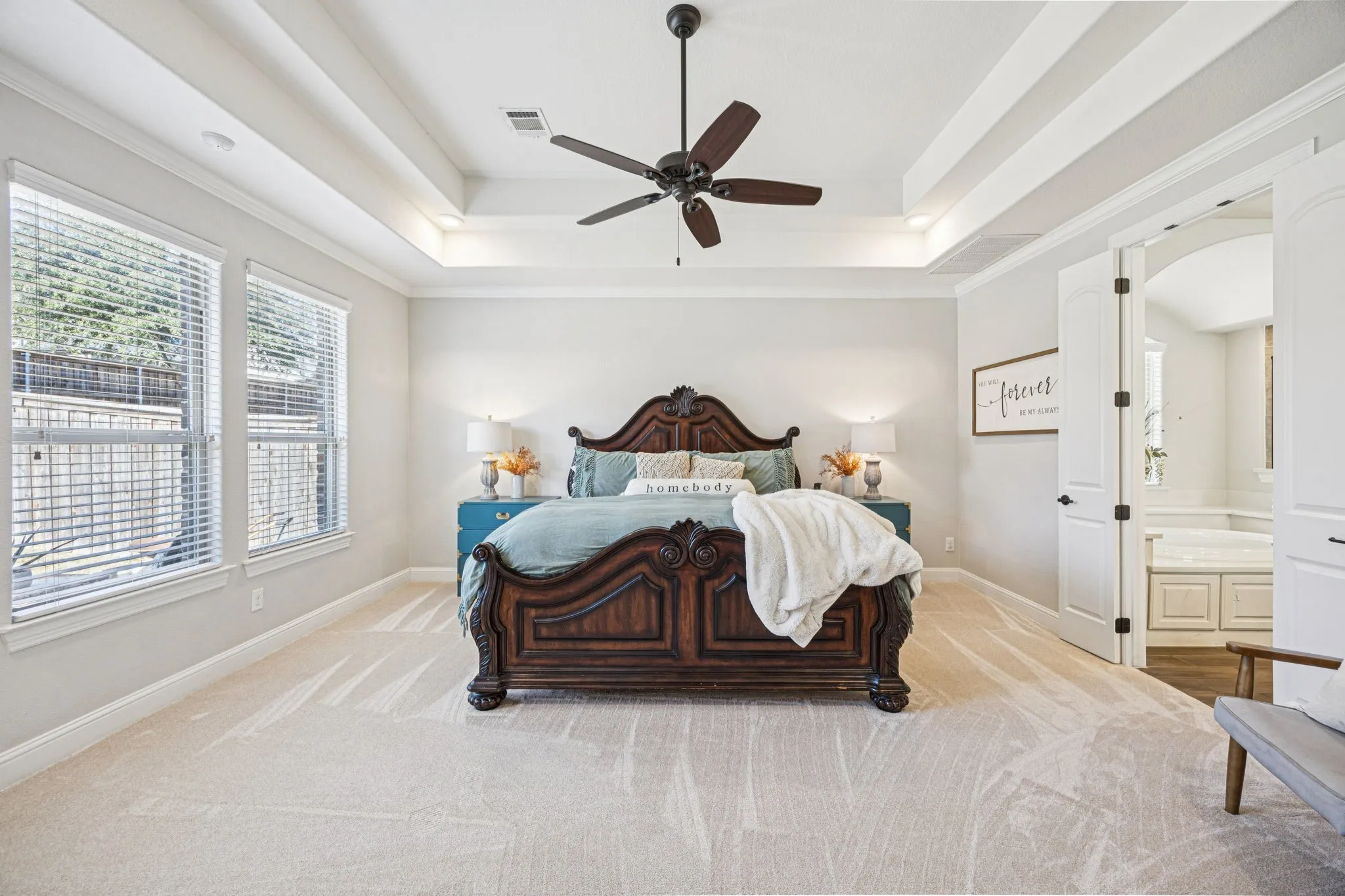 Recessed tray ceiling with crown molding, ceiling fan, carpeting, multiple windows with blinds, and white double doors opening to an arched doorway