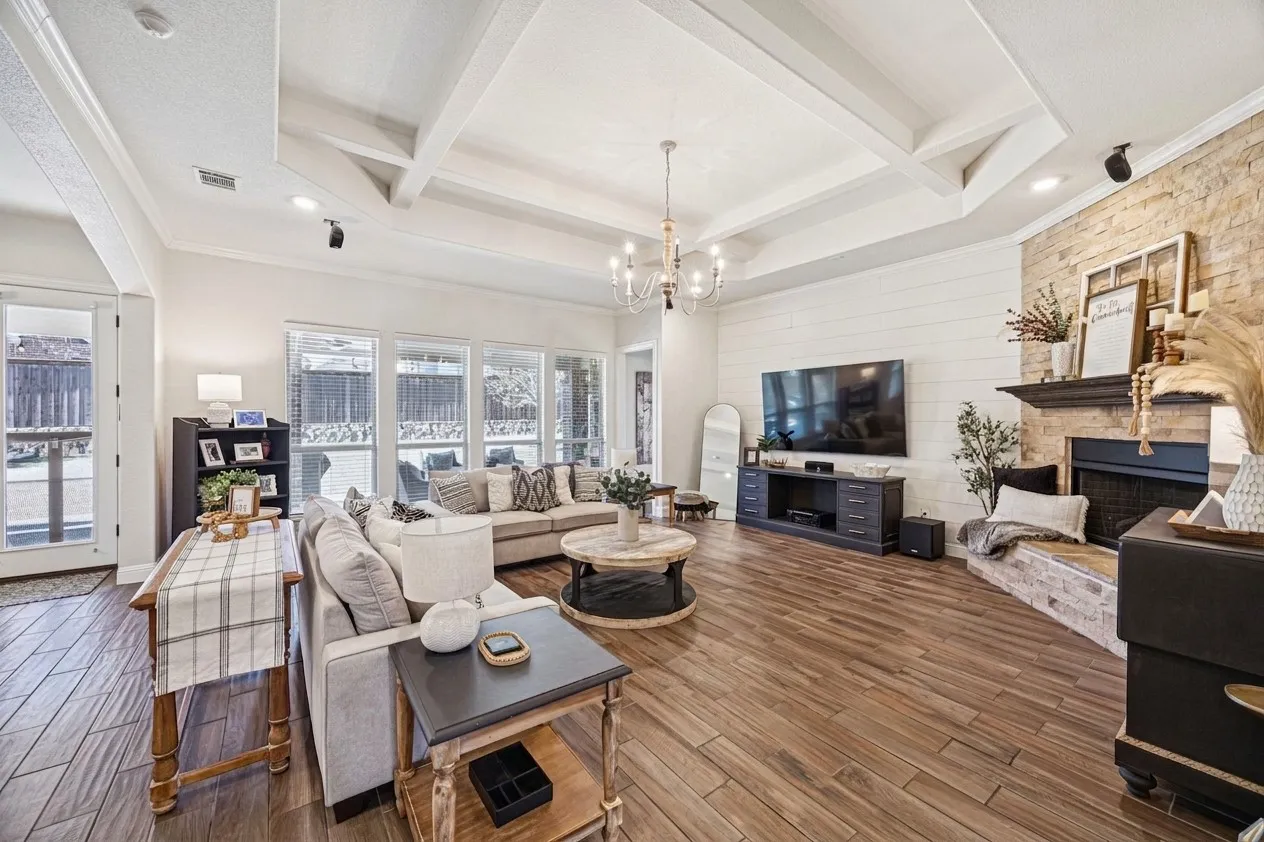 Coffered ceiling, wood-finish flooring, stone-accented fireplace, built-in shelving, and multiple windows