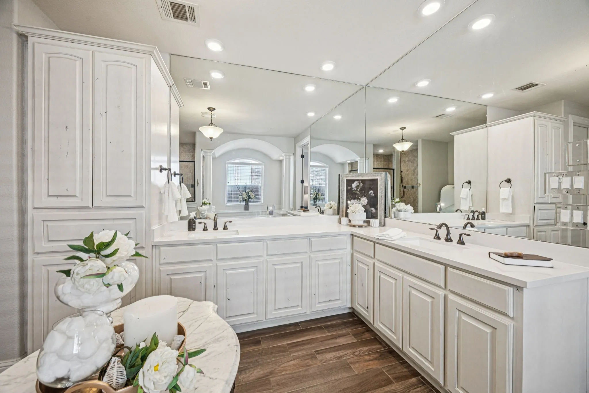 Dual vanity with white cabinetry, integrated sinks, dark bronze faucets, and extensive mirrored wall