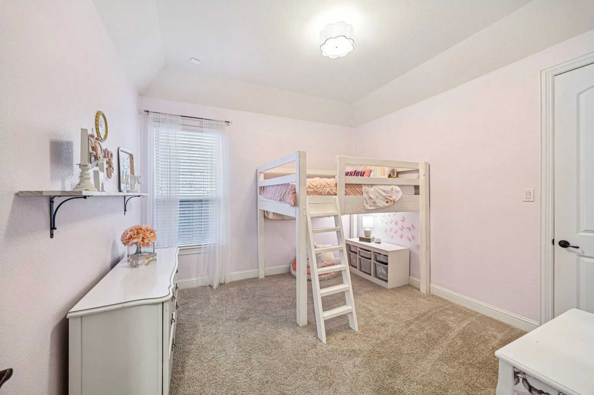 Vaulted ceiling, recessed window with blinds, wall-mounted shelf, carpeted flooring, and a flat-panel door