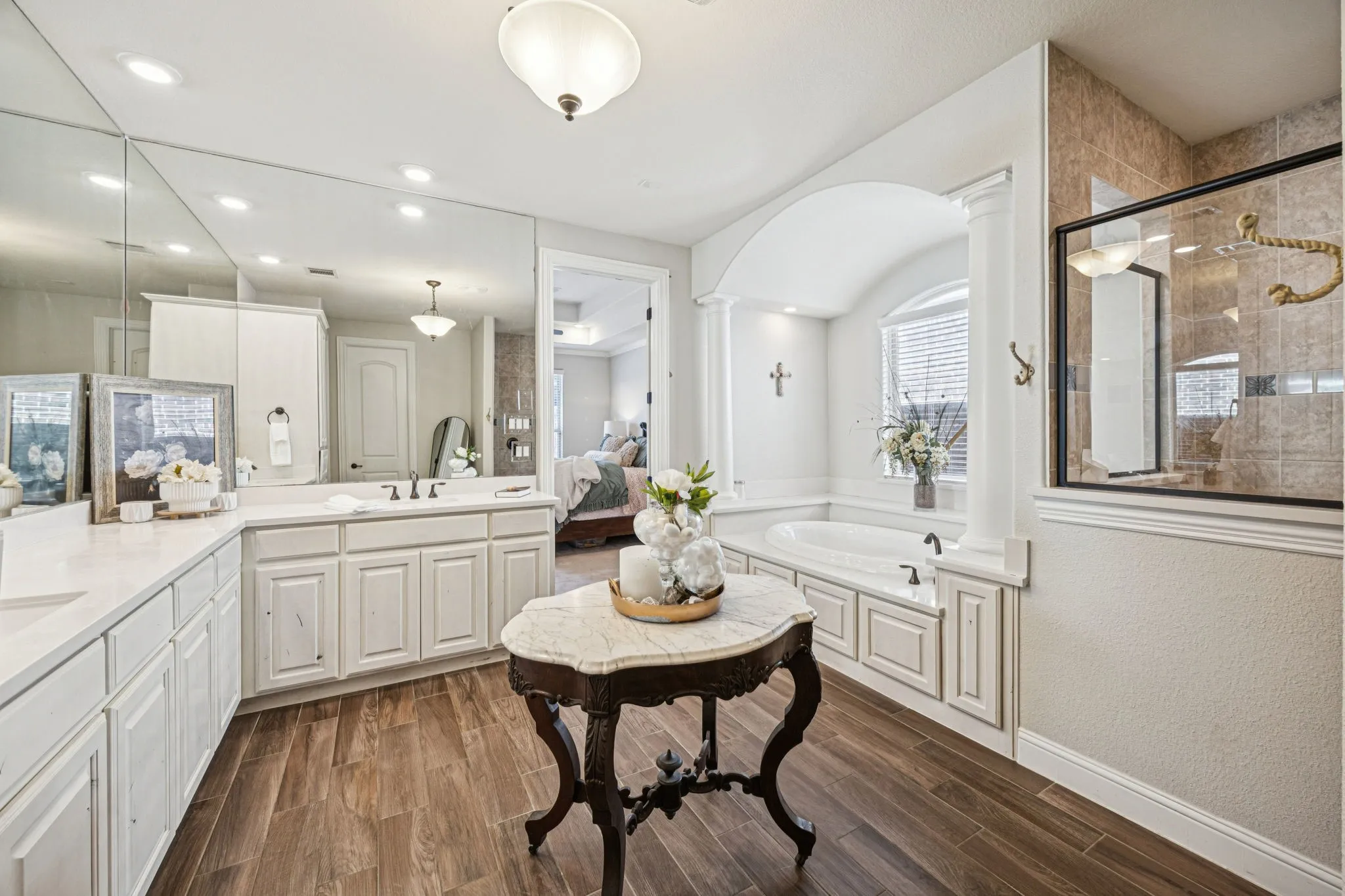 Spacious bathroom featuring wood-finish flooring, an expansive vanity with double sinks, a built-in soaking tub, and a separate glass-enclosed shower