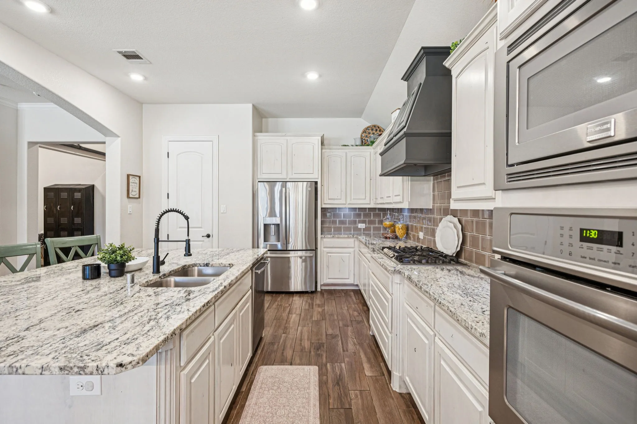 Kitchen featuring a substantial island with a dual-basin sink, wood-finish flooring, white cabinetry, stainless steel appliances, and granite countertops