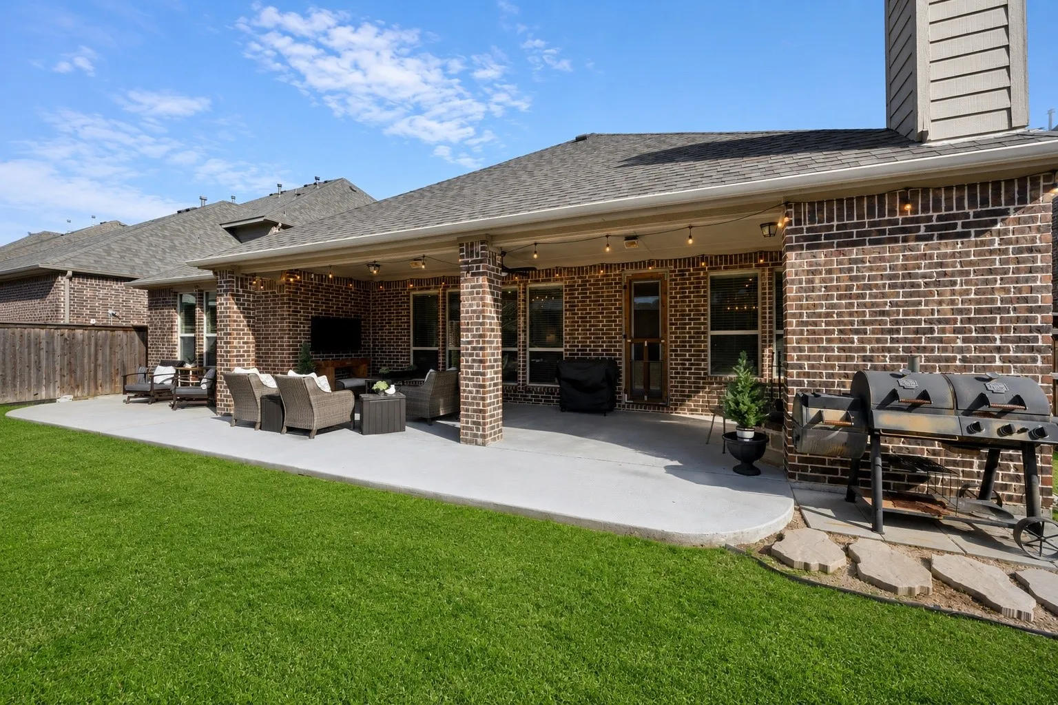 Expansive backyard featuring a covered patio, brick exterior, and a stone walkway