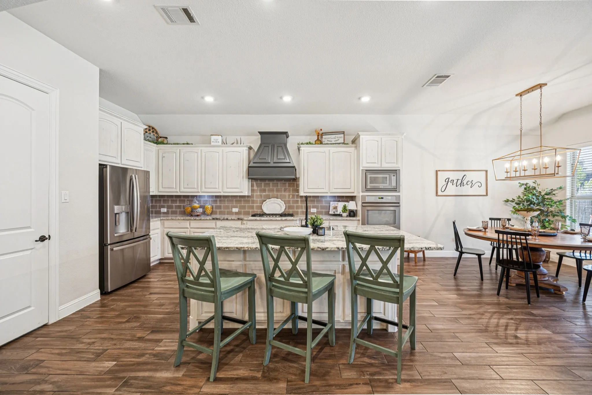 Spacious kitchen with a large central island, integrated stainless steel appliances, white cabinetry, and wood-finish flooring