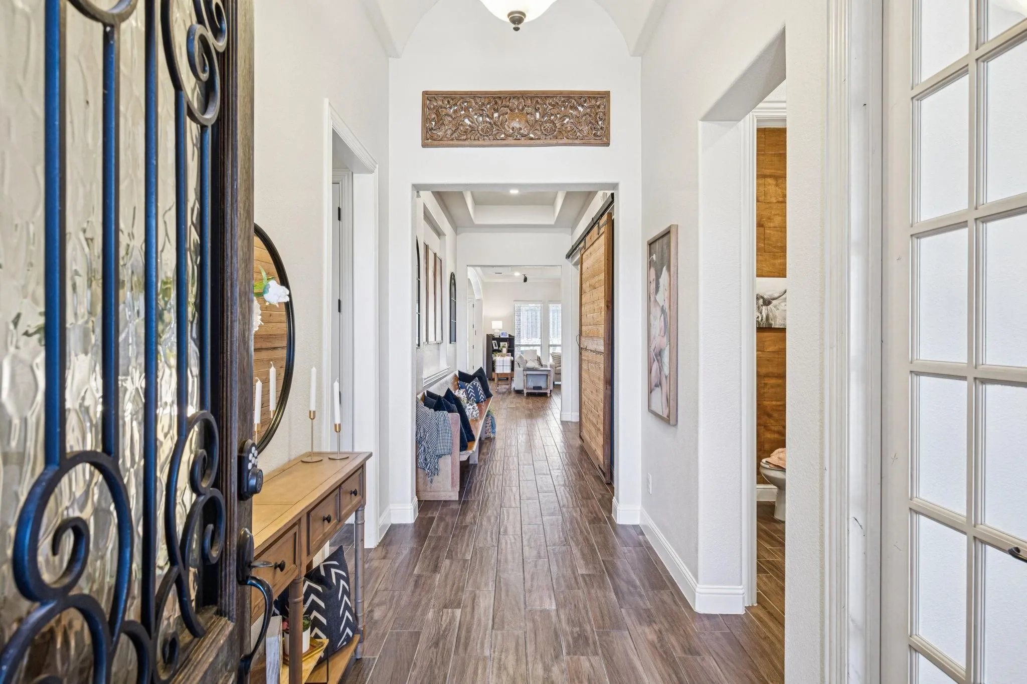 Arched entryway with a decorative wrought iron door, wood-finish flooring, recessed lighting, and a barn door accent