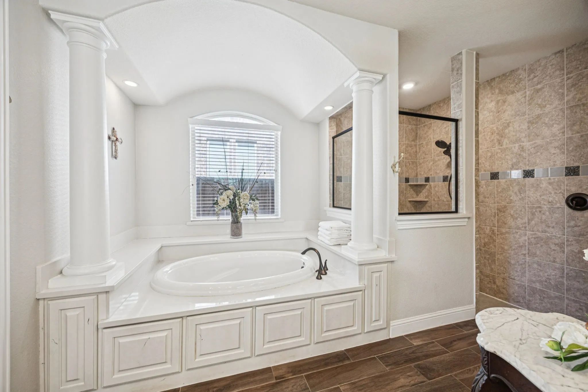 Soaking tub with a white surround and built-in cabinetry, accented by decorative columns and an arched alcove