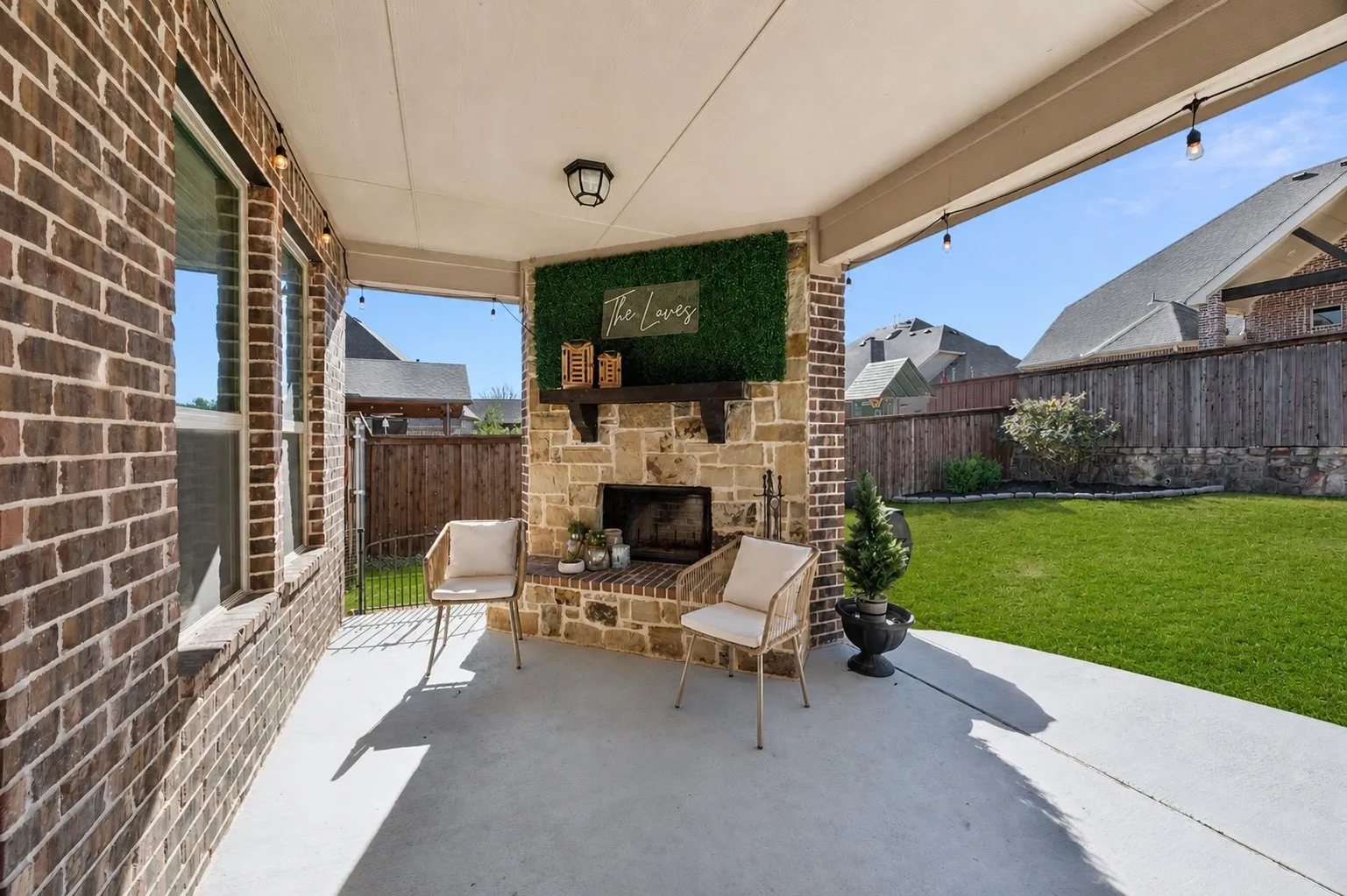 Covered patio featuring a stone fireplace with a wood mantle, brick accents, string lighting, and a concrete surface