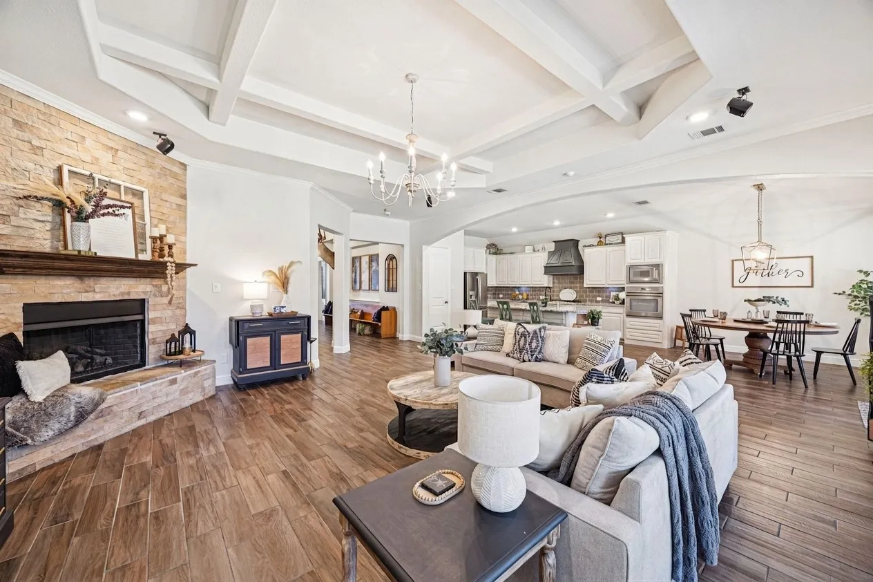Vaulted ceiling with exposed beams, stone-clad fireplace with hearth, wood-finish flooring, recessed lighting, and a chandelier