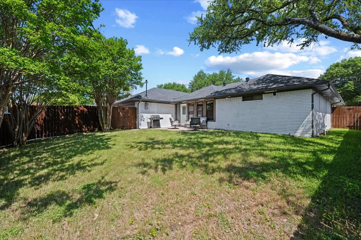 Expansive backyard featuring a manicured lawn, established trees, and a privacy fence