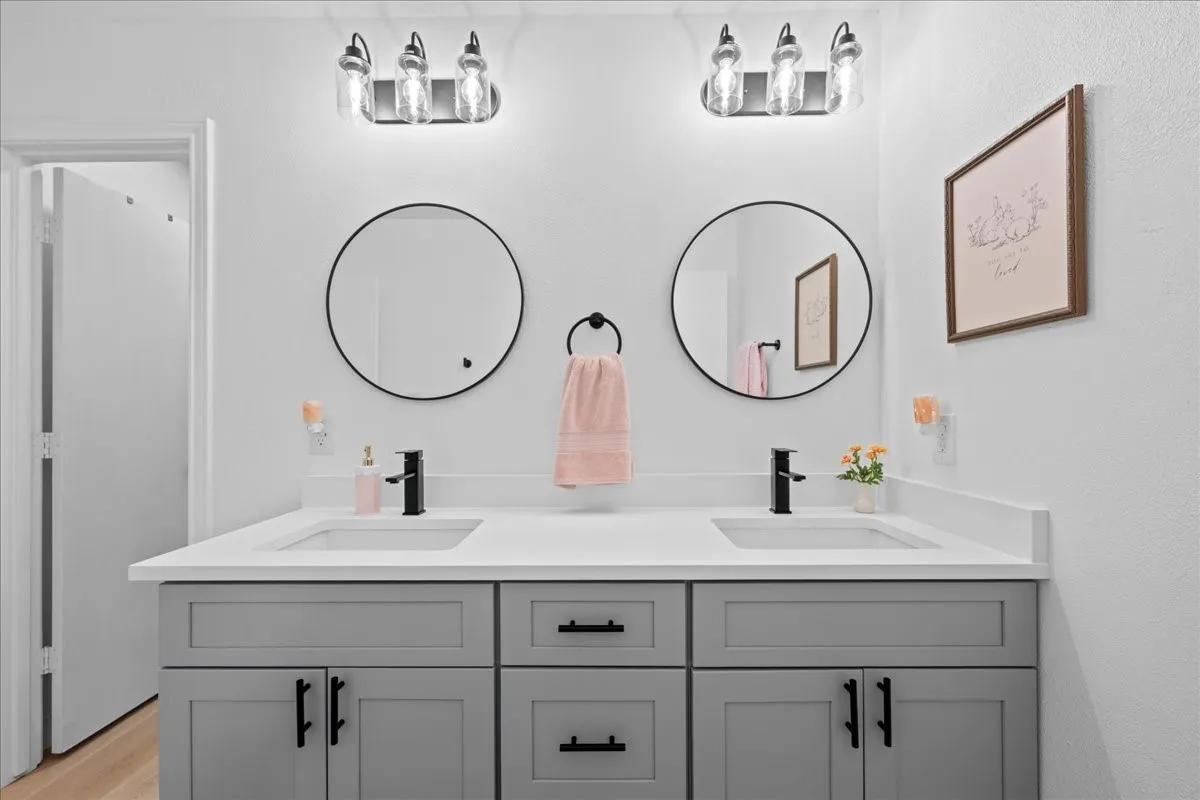 Dual vanity with a white countertop and undermount sinks, gray cabinetry with black hardware, and two circular framed mirrors