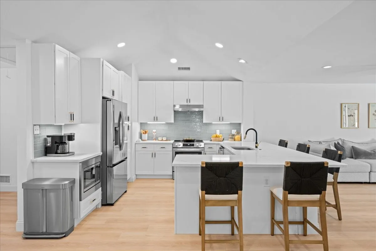 Vaulted ceiling, recessed lighting, white cabinetry, stainless steel appliances, and a central island with a sink