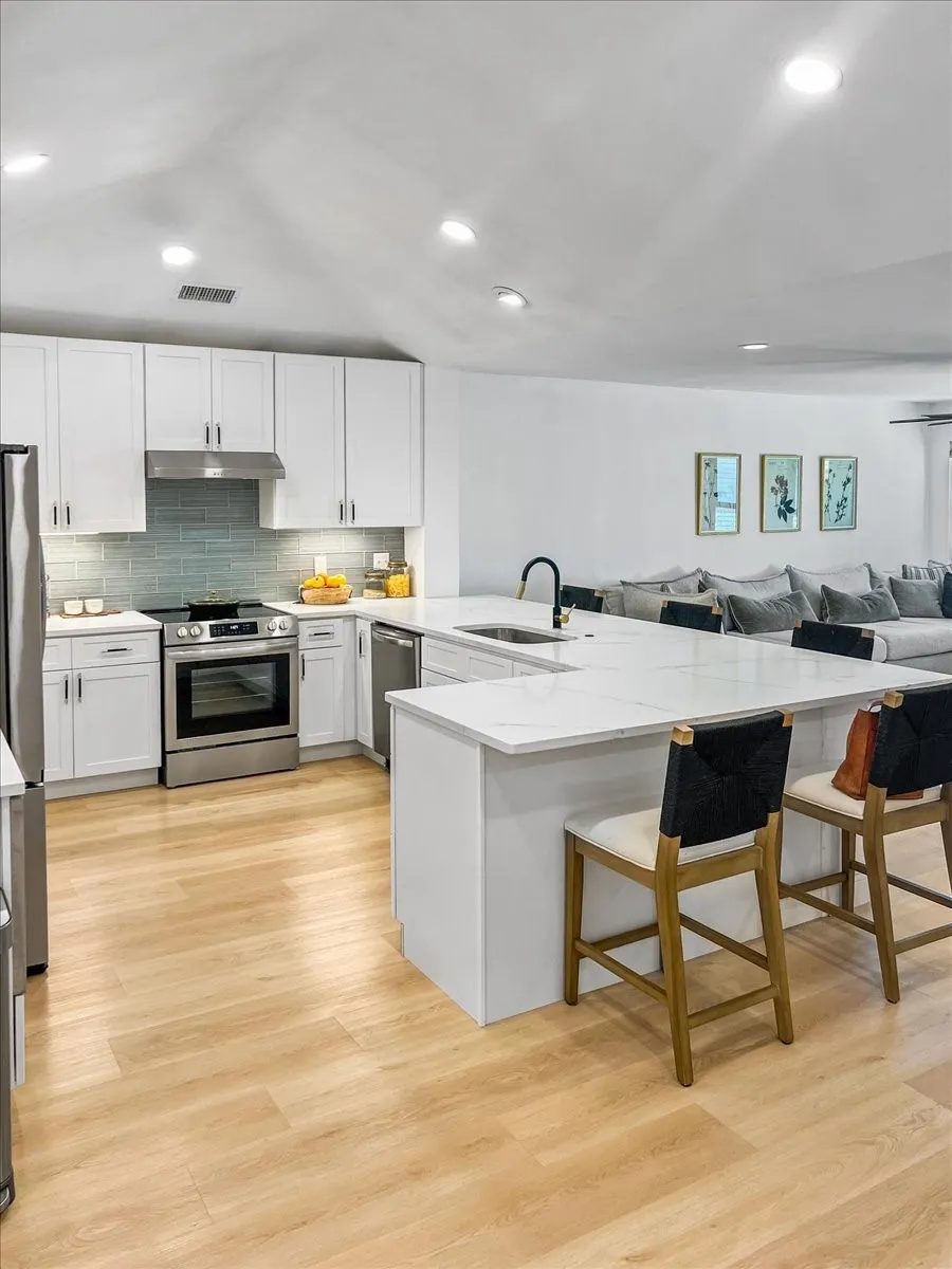 Kitchen featuring white shaker cabinetry, stainless steel appliances, a light-toned wood-finish floor, and a large central island with seating