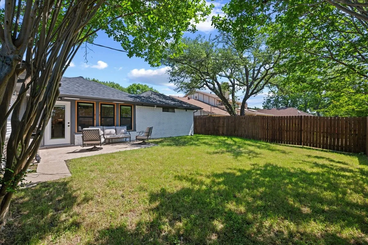 Expansive backyard featuring a concrete patio, a wood privacy fence, and mature trees