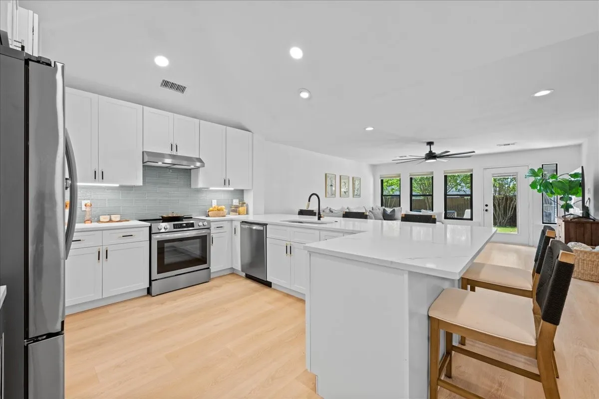 Modern kitchen featuring white cabinetry, light wood-finish flooring, stainless steel appliances, a large center island, and recessed lighting