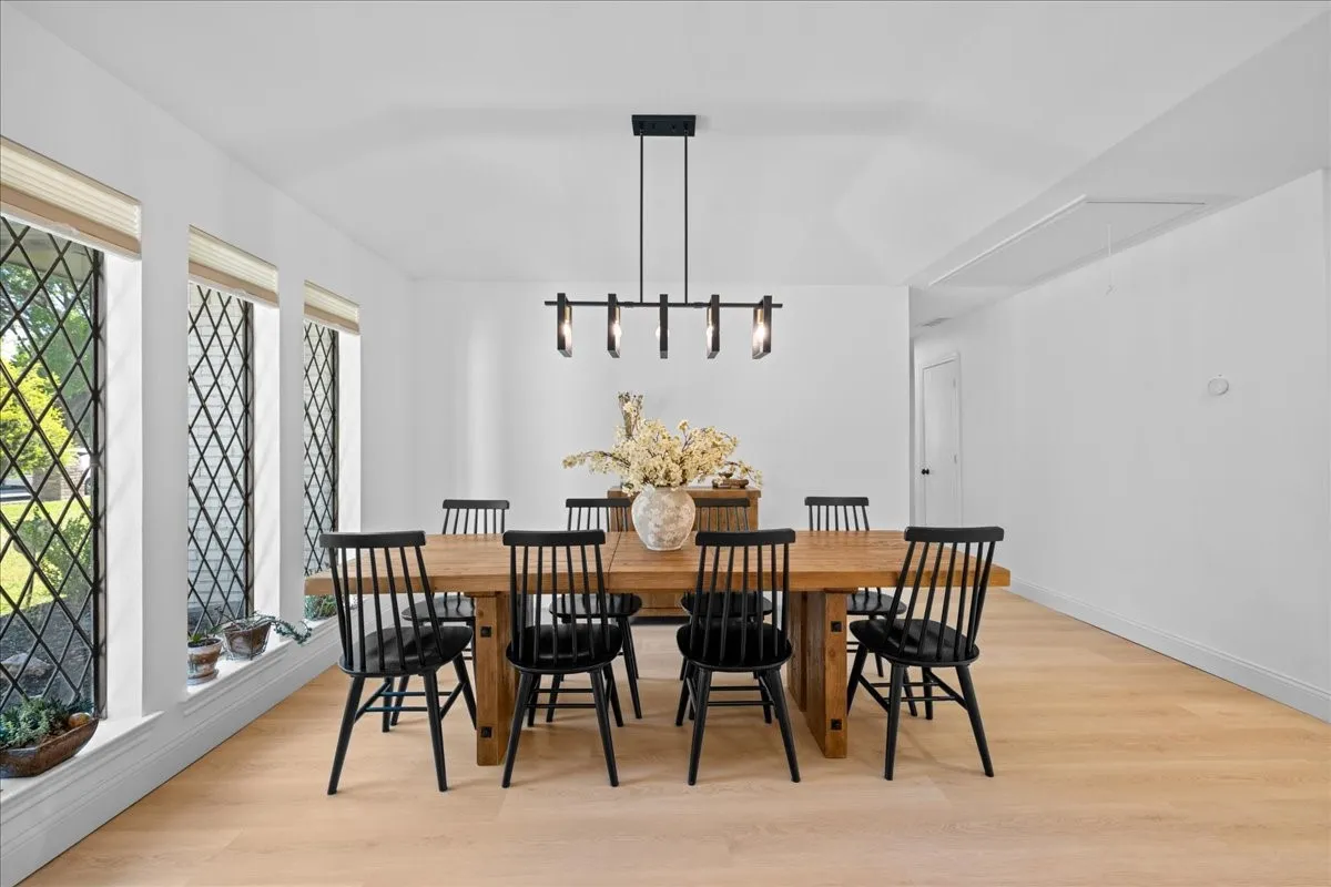 Vaulted ceiling with a linear chandelier, light wood-finish flooring, and multiple lattice-pattern windows